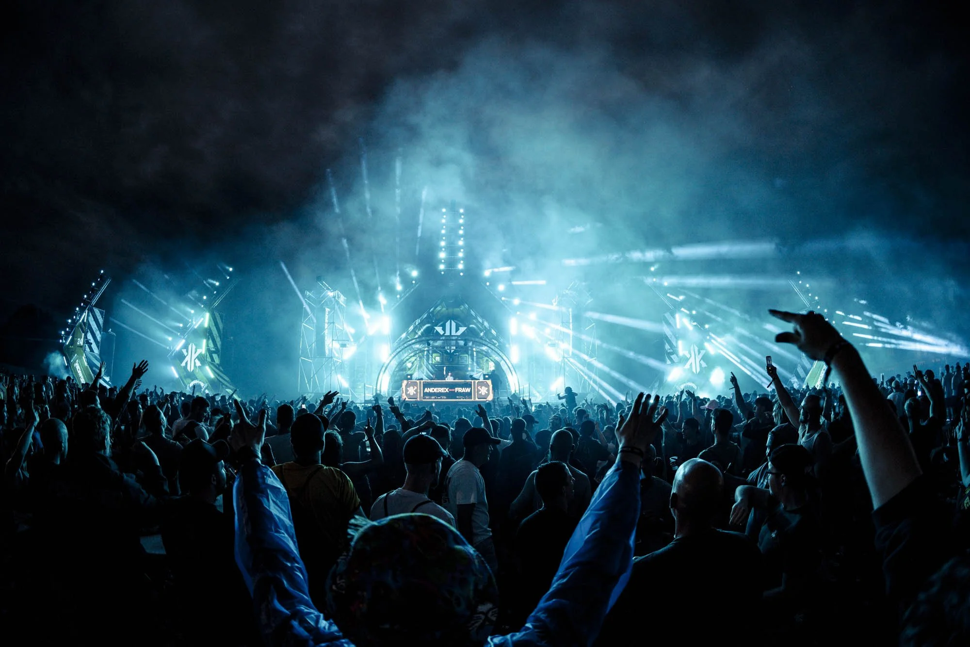 Menschen feiern auf einem Konzert mit hellen blauen Lichteffekten und einer Bühne im Hintergrund.
