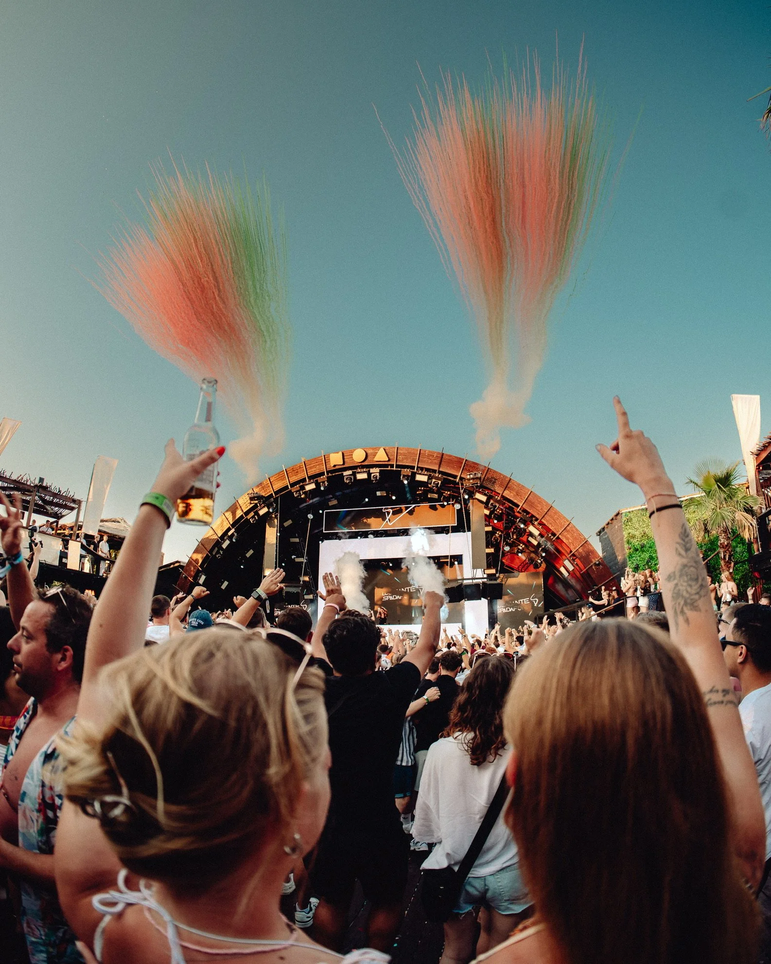 Festivalbesucher vor einer Bühne mit Rauch und bunten Pulverexplosionen am Himmel.