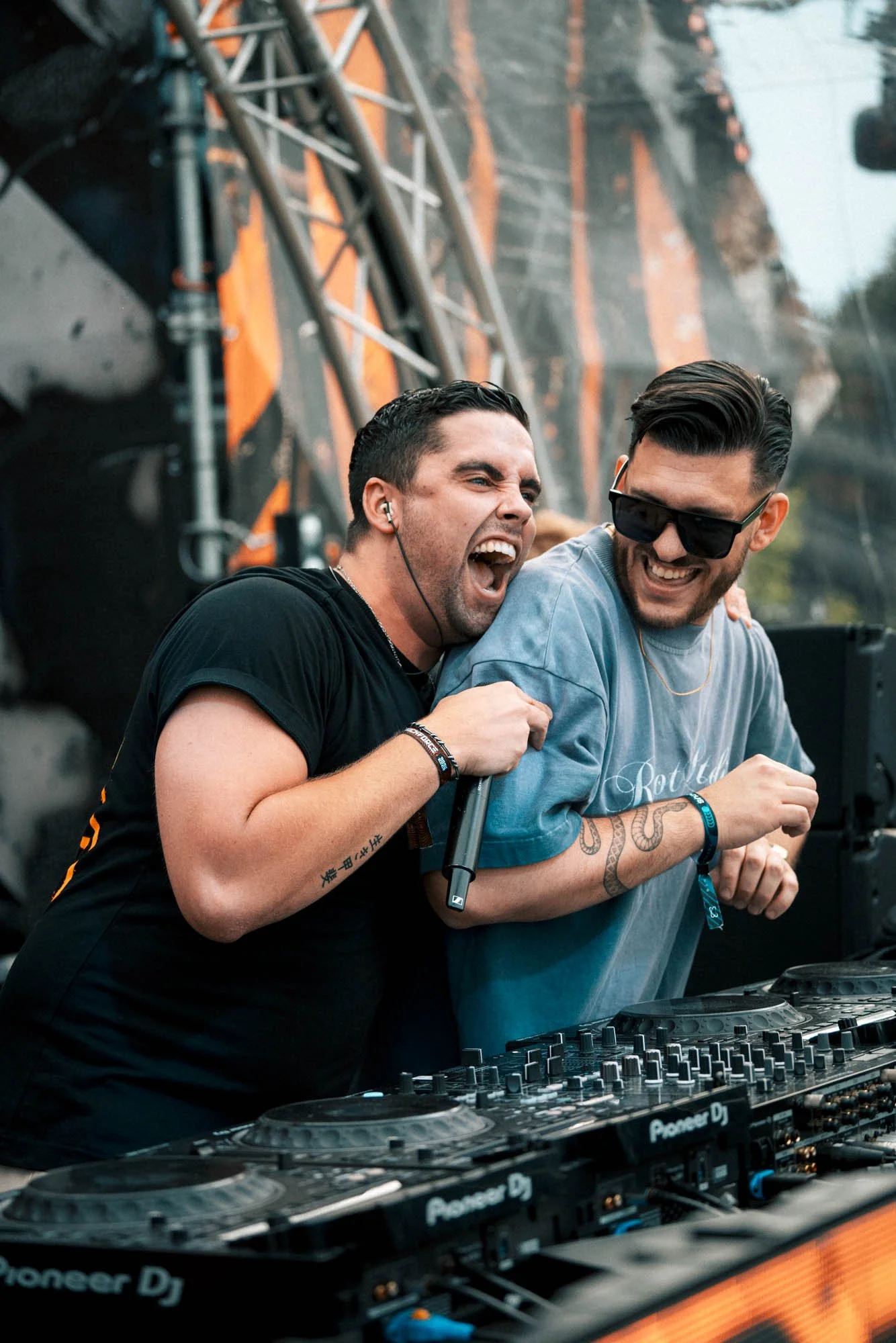 Zwei Männer beim DJ-Auftritt, lachen und feiern mit DJ-Equipment auf der Bühne.