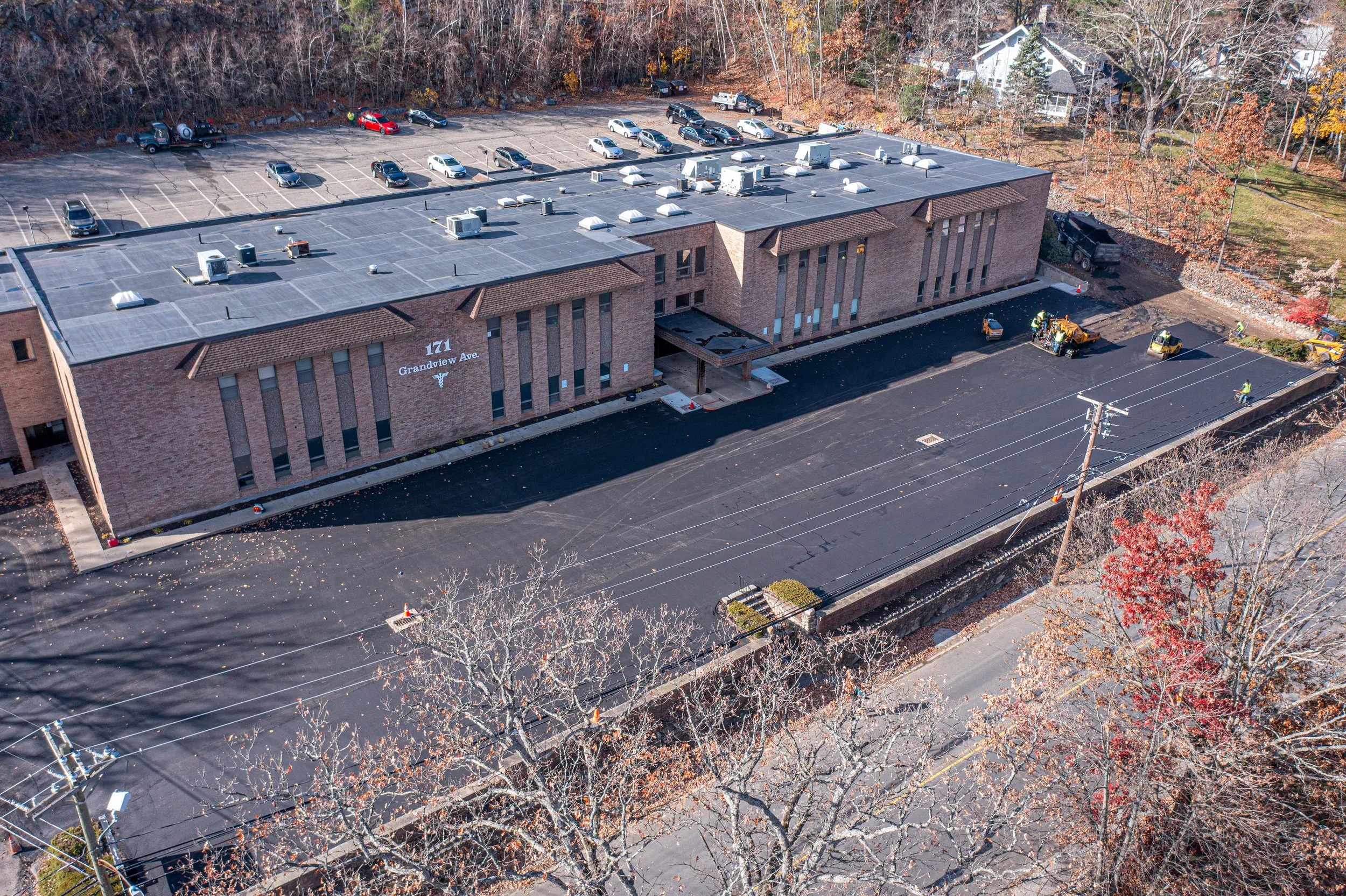 An aerial view of a brick apartment building with a parking lot and trees with fall foliage.