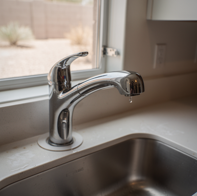 Chrome kitchen faucet with dripping water over a sink near a window and door.