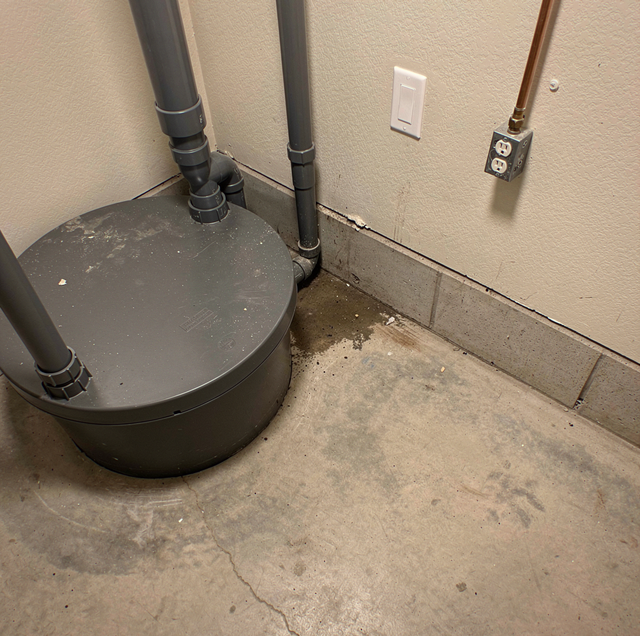 Round tank with pipes against a wall with a light switch and electrical outlet above.