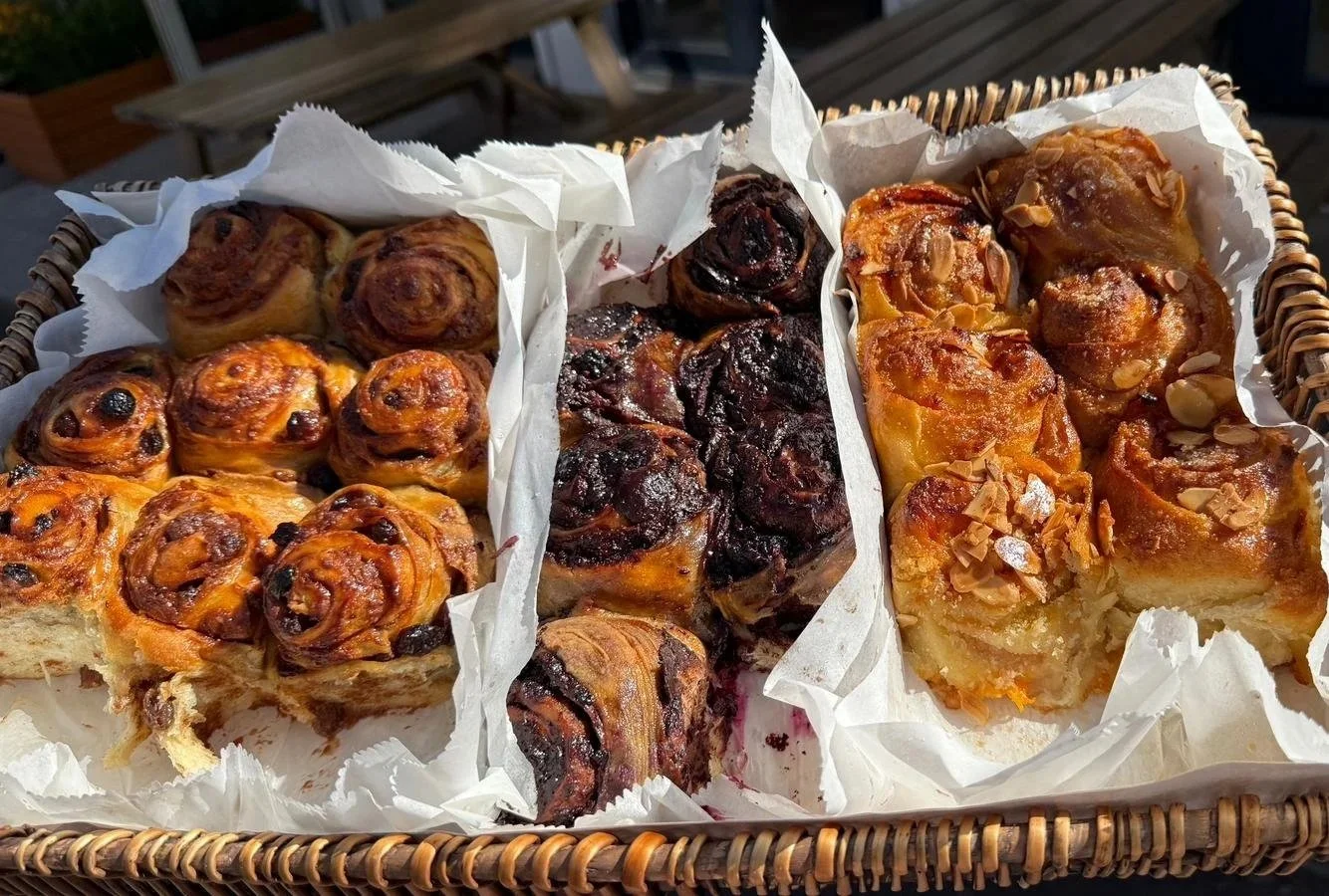 A basket filled with assorted homemade baked buns, including cinnamon tahini, chocolate and almond & ricotta.