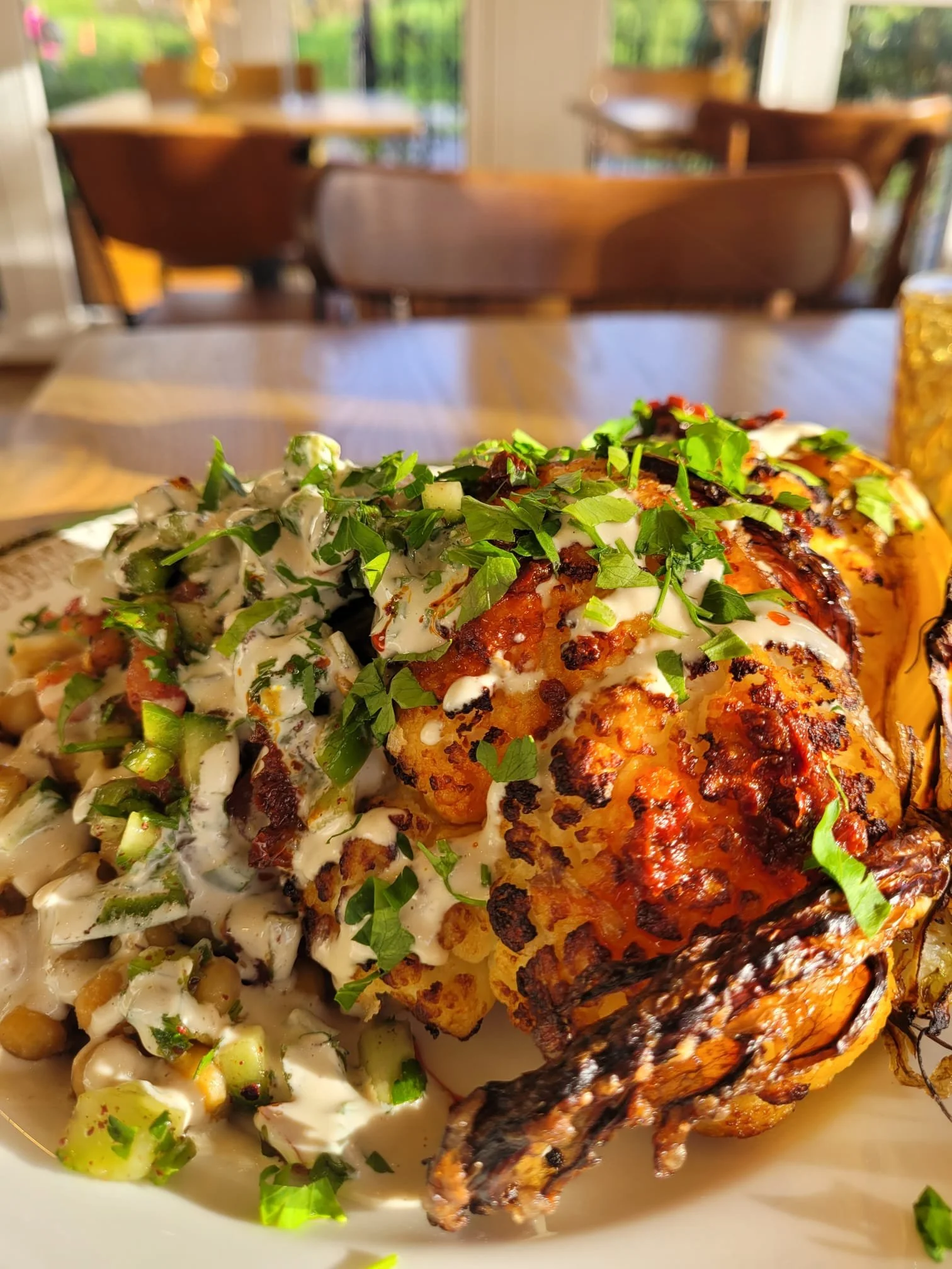Close-up of a plate with roasted cauliflower topped with chopped green herbs and a side salad with herbs.