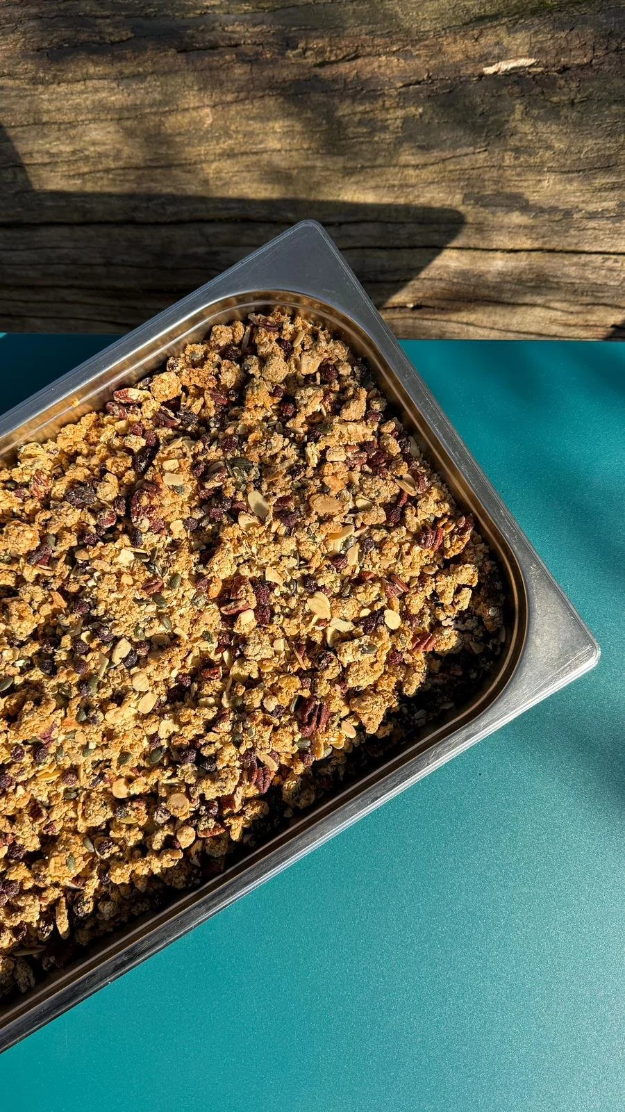 Close-up of a tray of freahly baked granola filled with nuts, oats, and dried fruits on a teal surface.