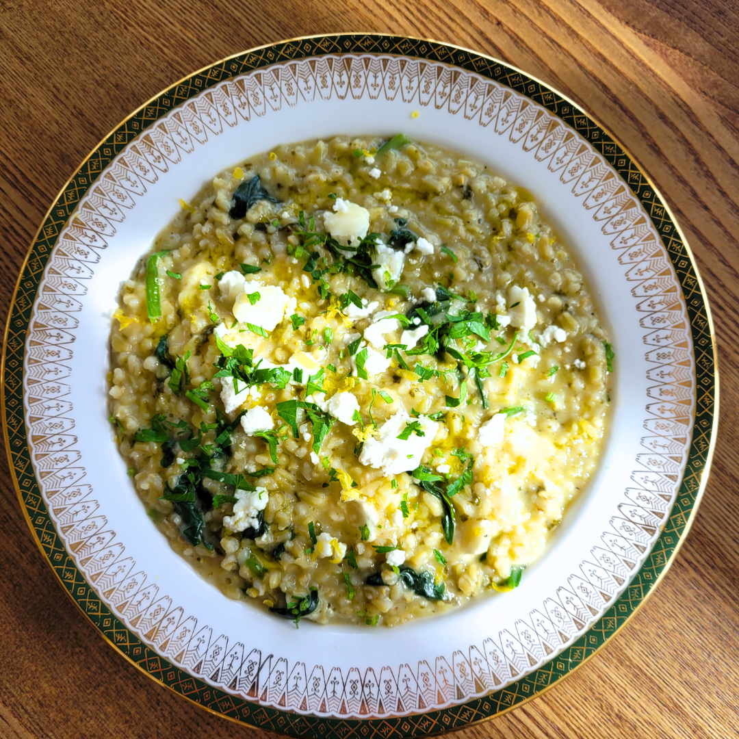 A bowl of creamy risotto with chopped herbs, crumbled cheese, and yellow zest on top, served on a decorative plate.
