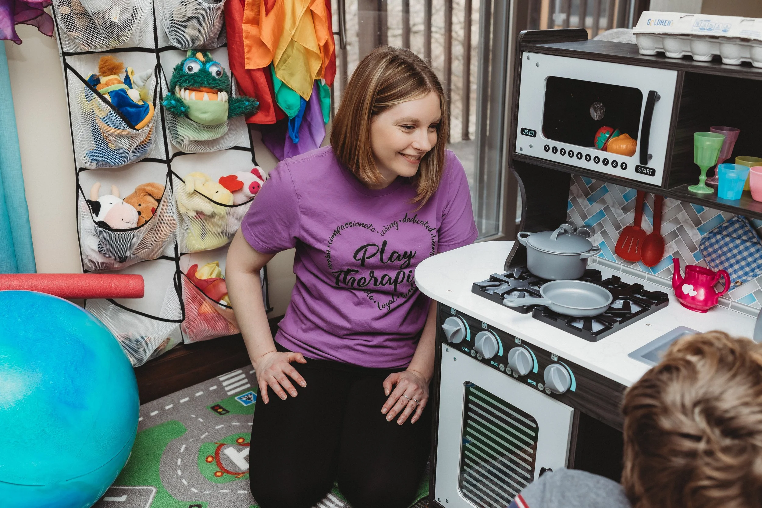 therapist smiling at child during play therapy while child plays with toy kitchen
