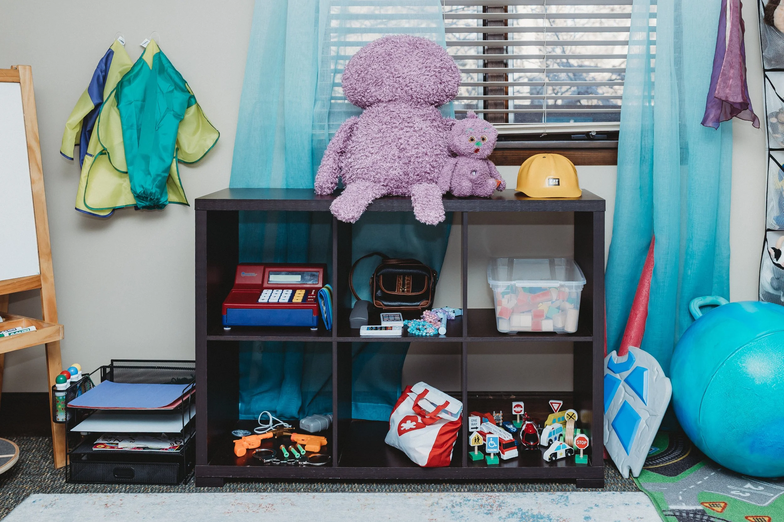 shelf of play therapy toys including ball, shield, cash register, weapons, blocks, vehicles, and doctor's kit
