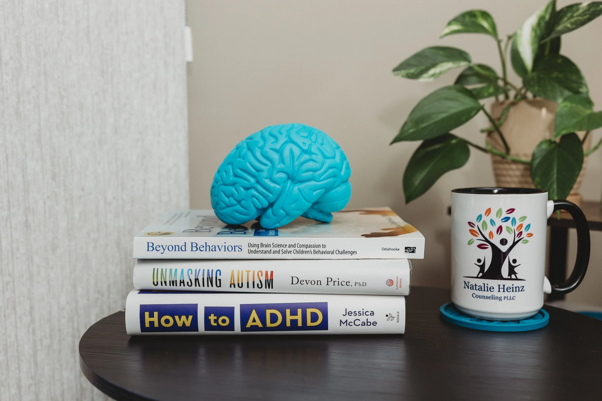 Neurodivergent Therapist Therapy for Neurodivergent Image of a stack of books about autism and ADHD with a book brain on top and a coffee mug of Natalie Heinz Counseling logo
