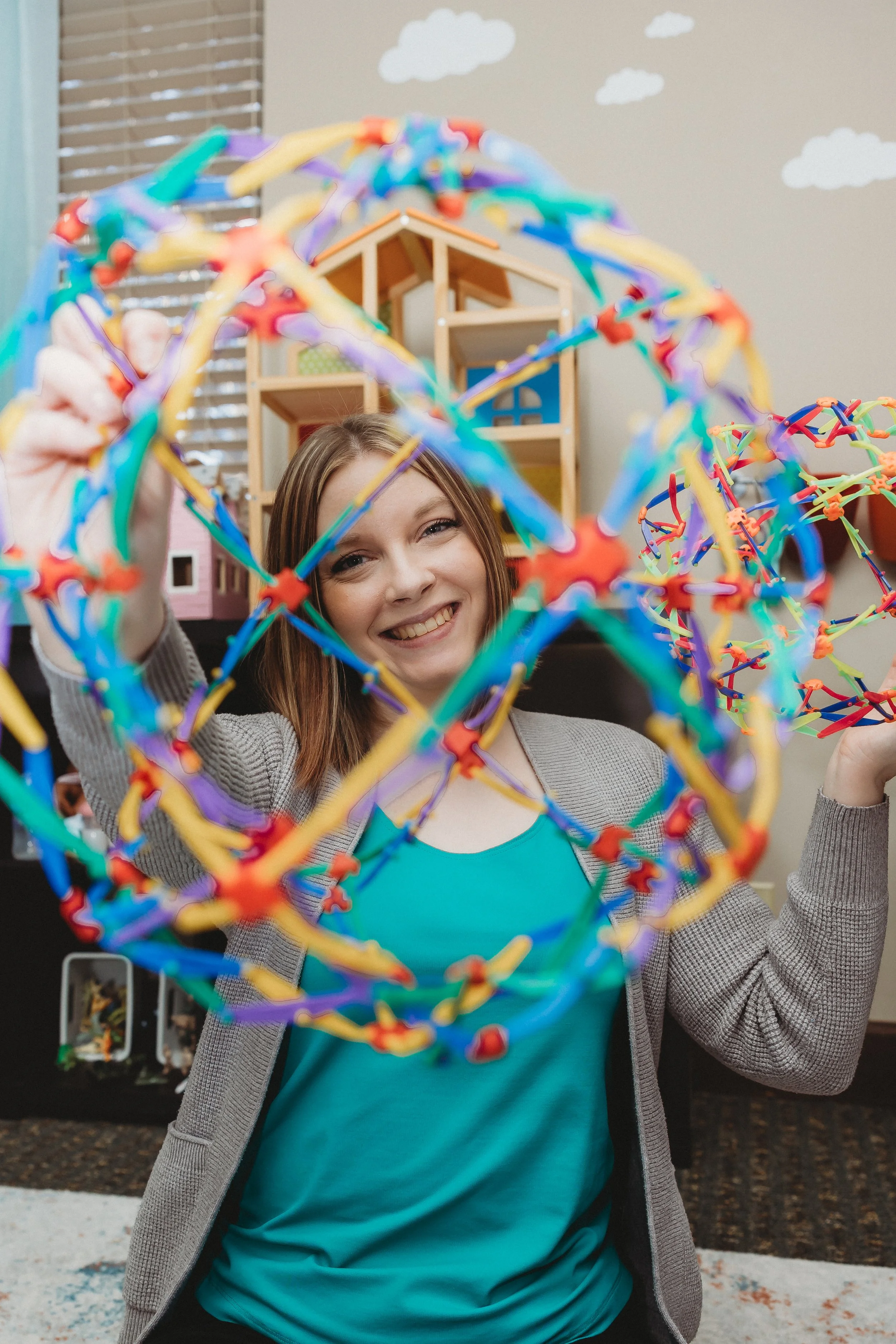 Peoria Play Therapist Natalie Heinz Counselor Image shows Natalie smiling looking through a colorful hoberman sphere