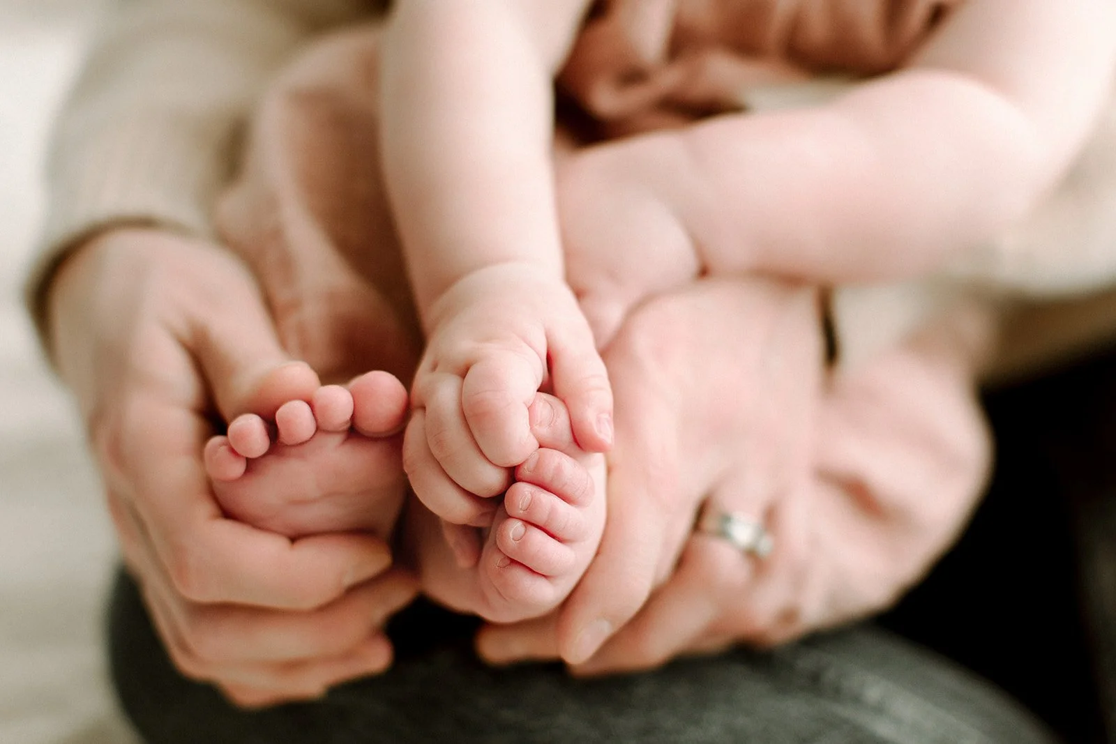 Close-up of an adult holding a baby's feet with both hands, emphasizing the tenderness and care for postpartum mothers when they come to pelvic floor therapy.