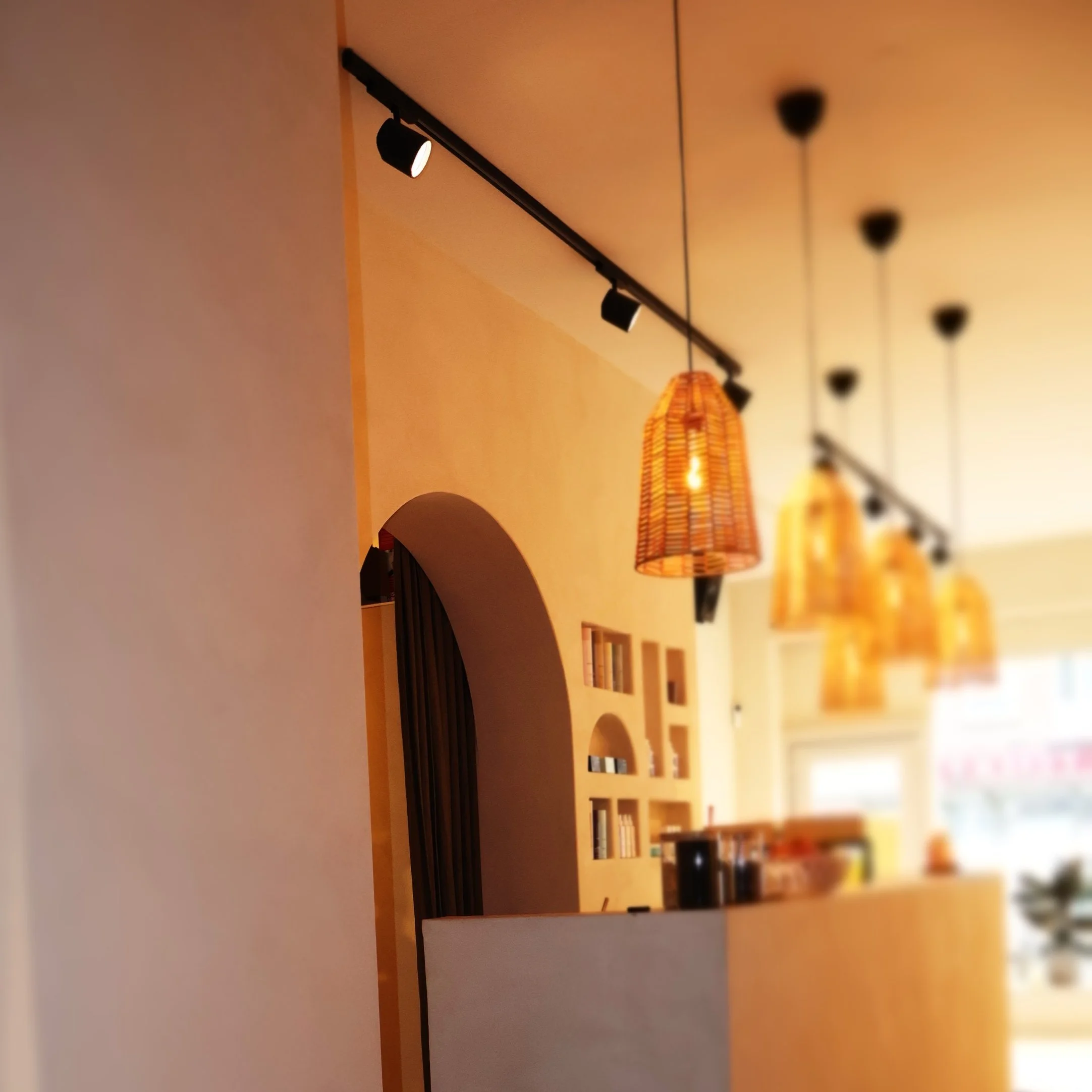 Interior of a modern cafe with wicker pendant lighting, track lighting, arched wall cutouts with shelves, and a counter.