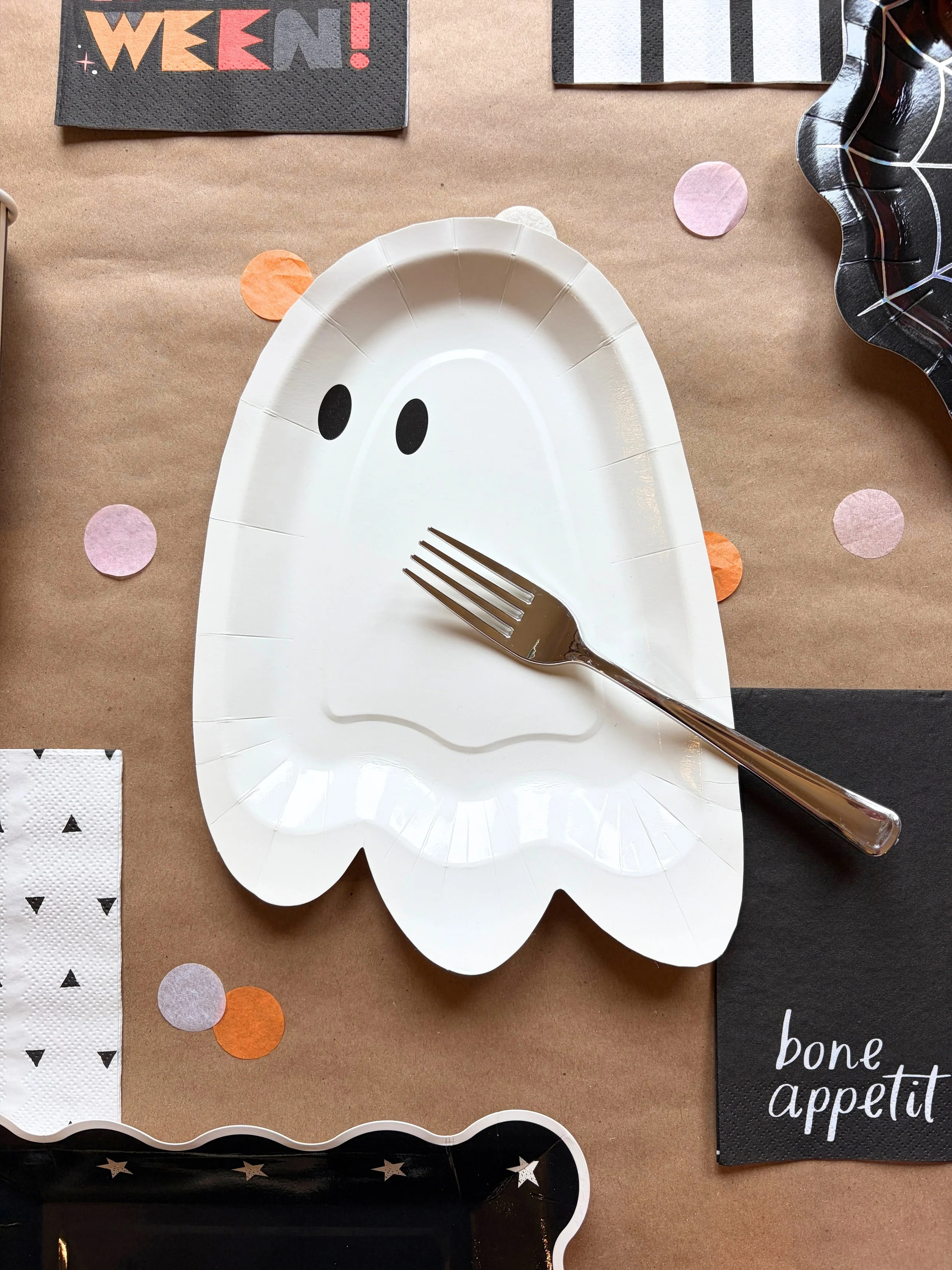 Classic Boo Halloween tableware close-up with ghost plate, silver fork, confetti, and colorful halloween napkins