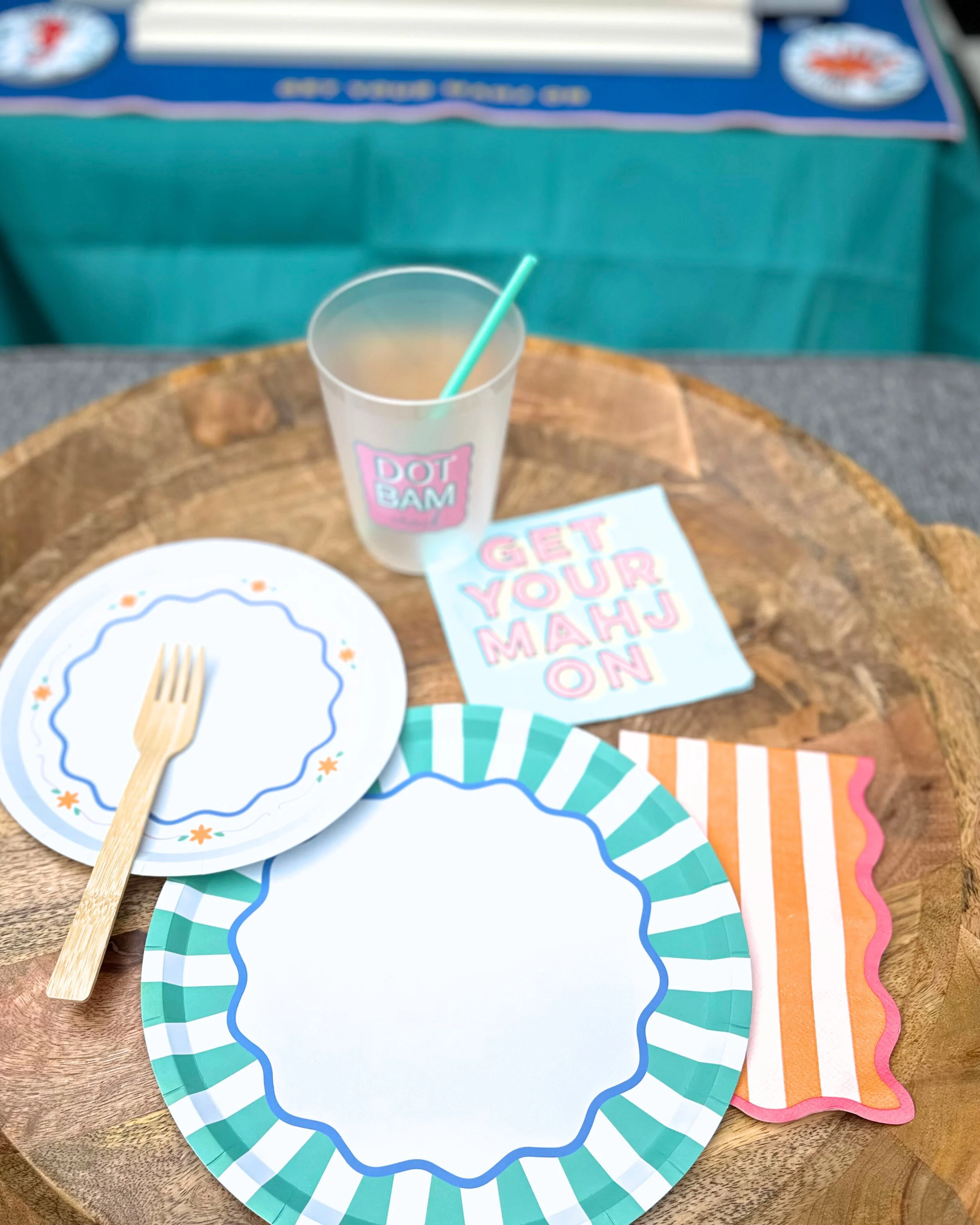 Mahjong party place setting with colorful and modern plates, reusable cup, straw, and patterned napkins.