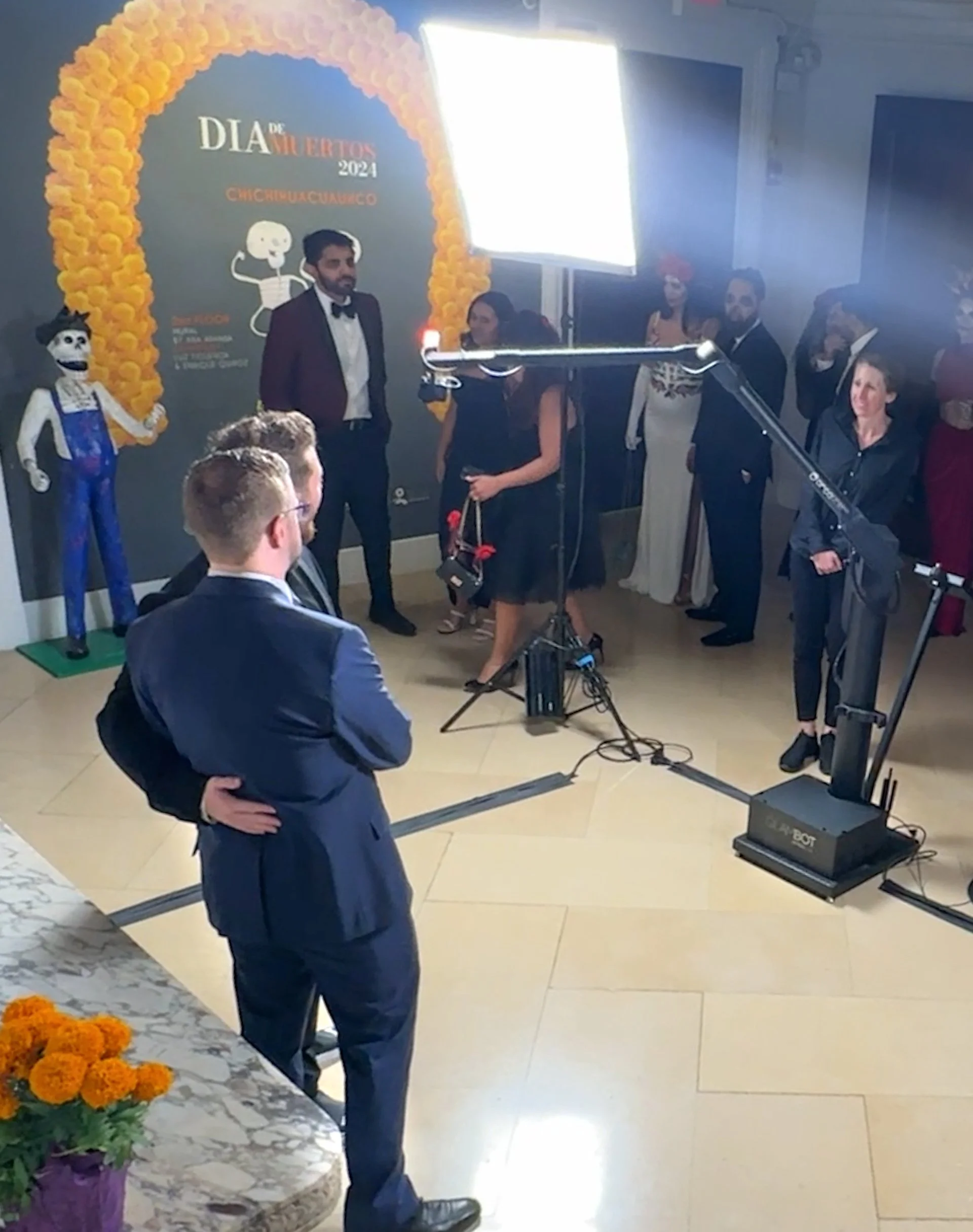 People celebrating Día de Muertos 2024 event with skeleton decorations, flowers, and participants in formal attire.