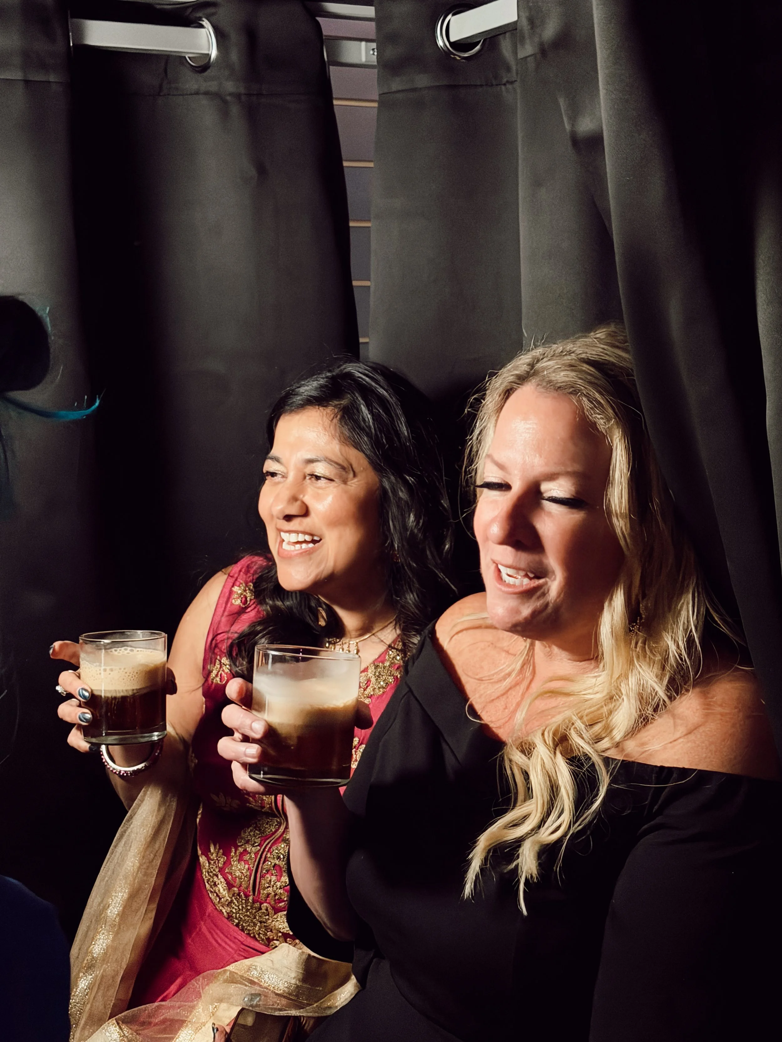 Two women smiling and holding glasses of beer at a social gathering or celebration.