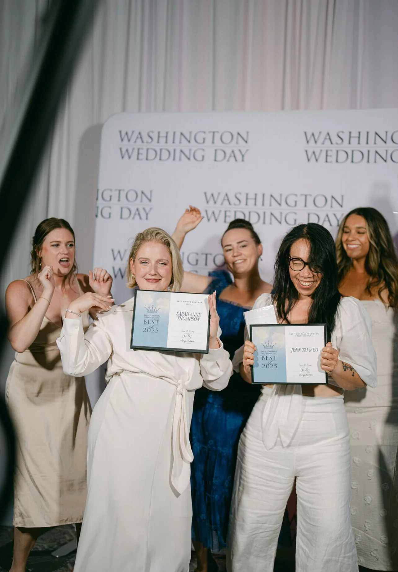 Group of women celebrating at a wedding event, some holding certificates for 'Best' awards in 2025, in front of a backdrop that reads 'Washington Wedding Day' multiple times.