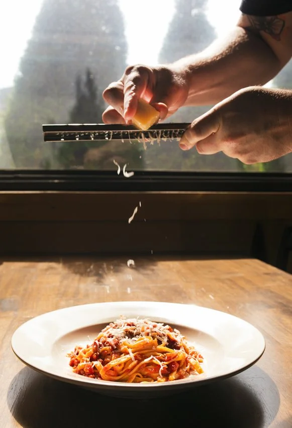 cheese being grated onto a pasta dish