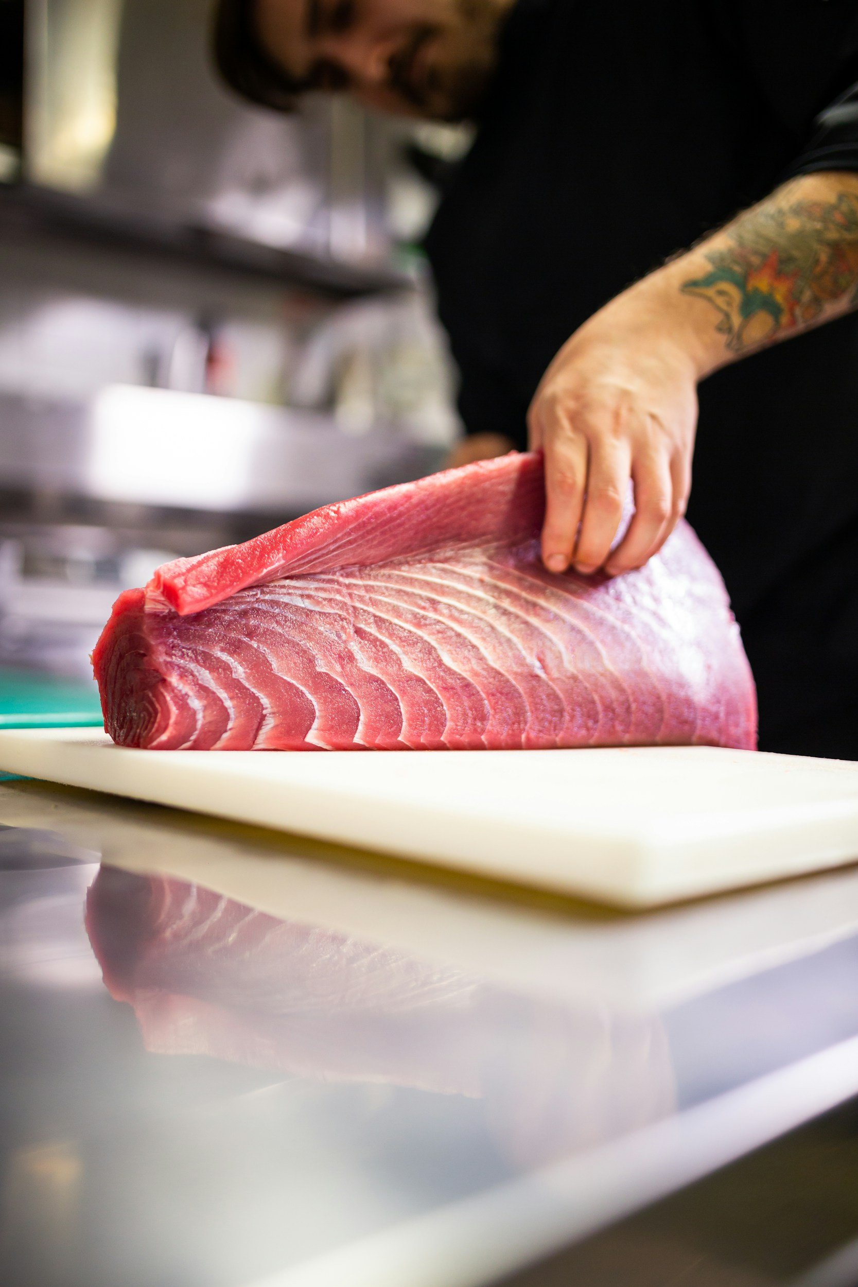 A person handling a large piece of fresh, raw tuna fish on a white cutting board in a professional kitchen.