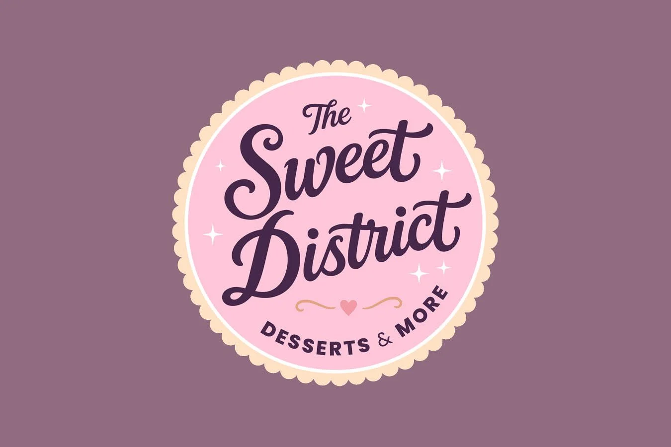 Logo for The Sweet District, featuring a pink circle with scalloped edges, decorated with small white stars. The text inside reads 'The Sweet District' in purple cursive, with 'Desserts & More' underneath in smaller purple font, and a small pink heart with accent lines below.