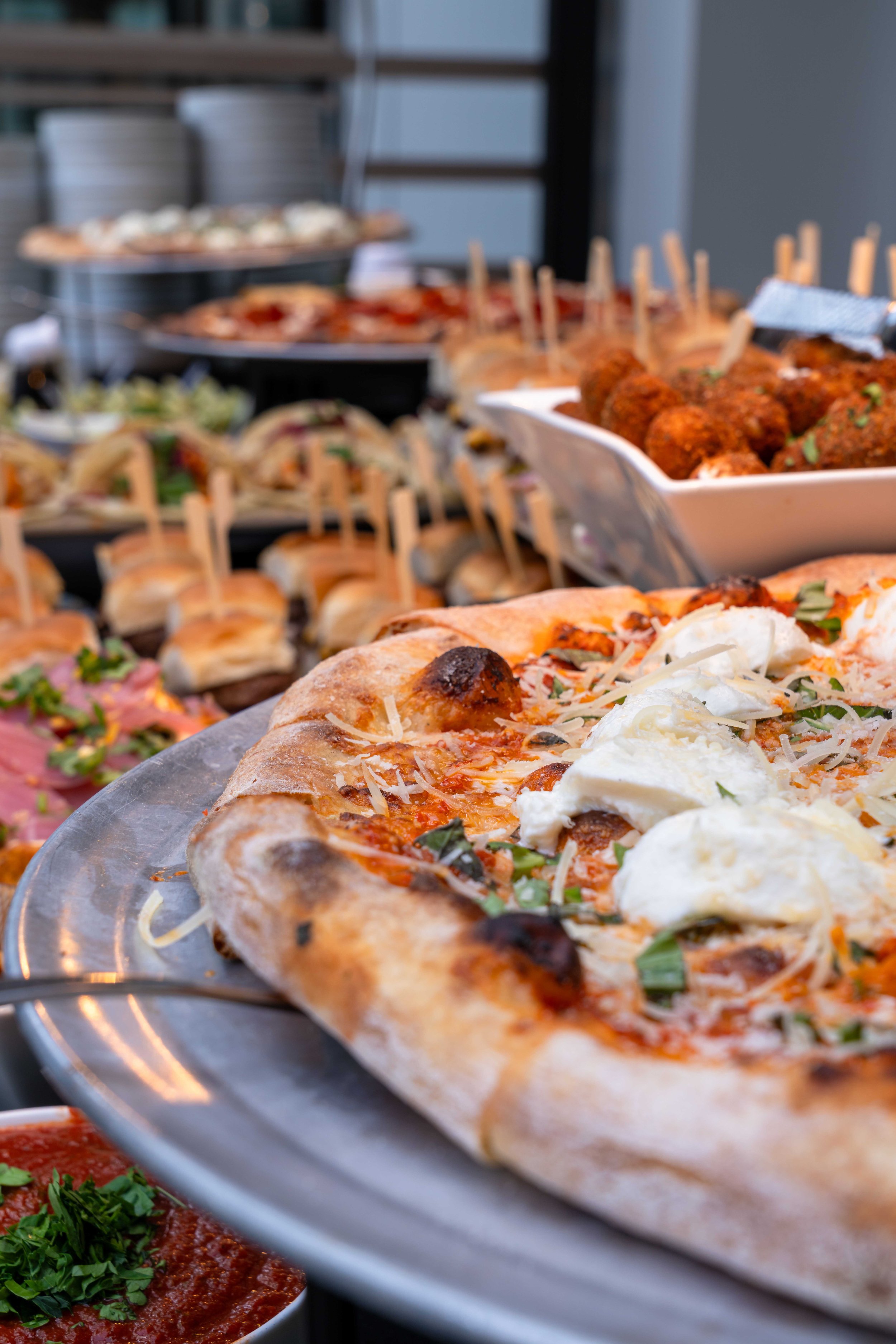 Close-up of assorted pizzas, including cheese and pepperoni varieties, on a metal tray.