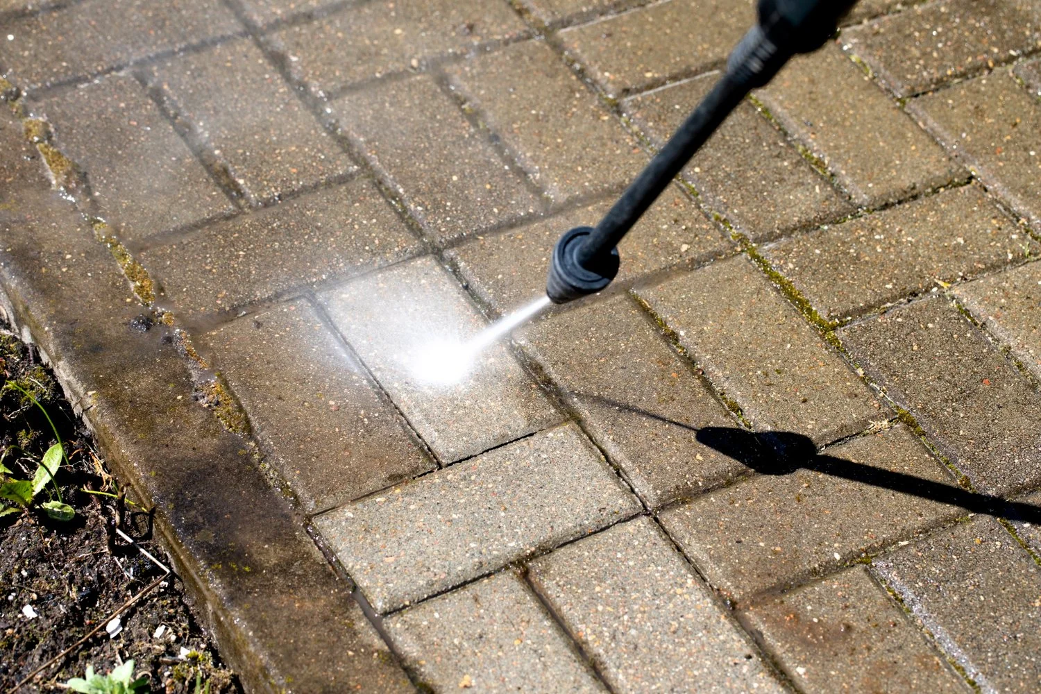 A pressure washer cleaning a brick pavement walkway with water spray.