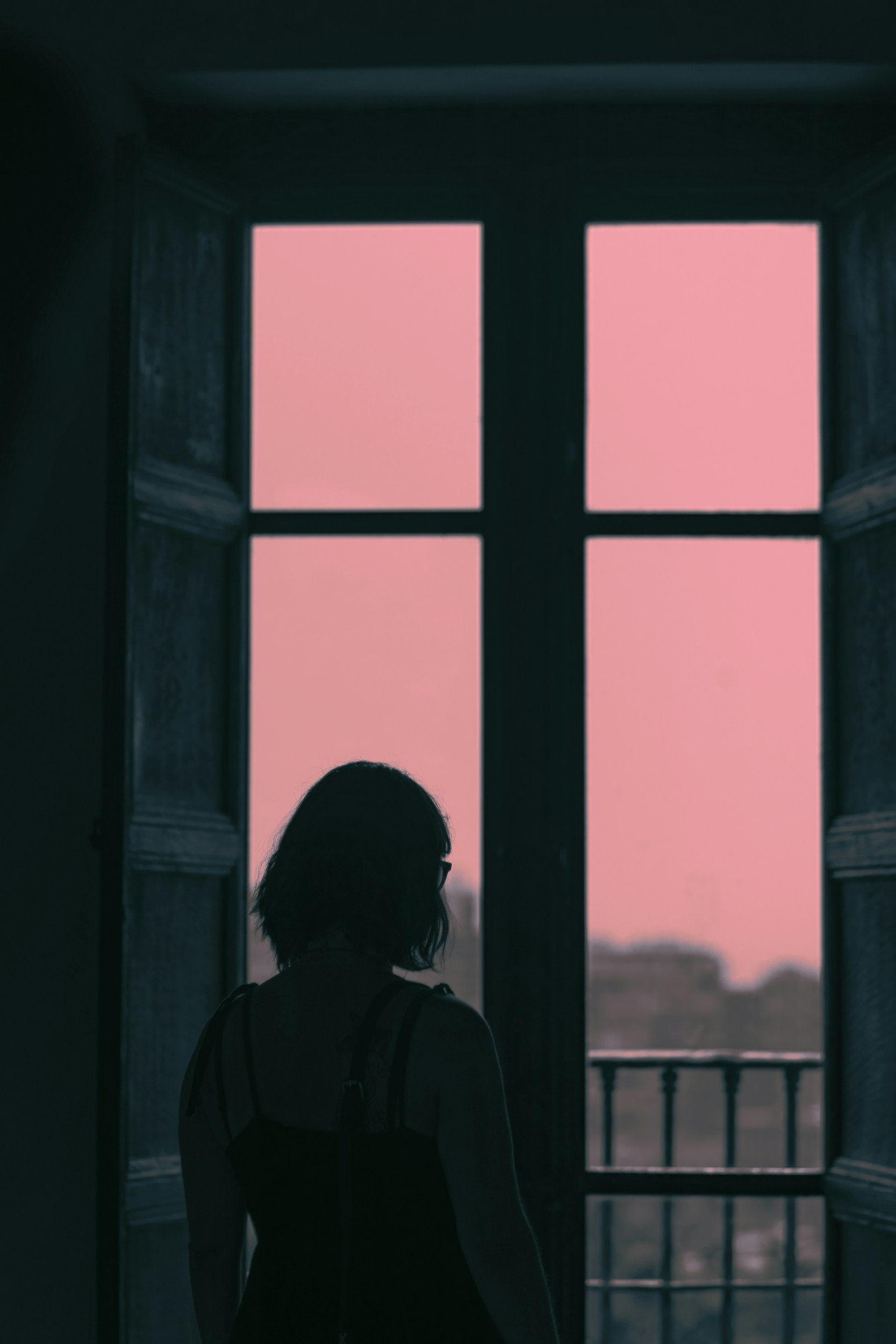 Silhouette of a woman with short hair and glasses looking out a window at sunrise.