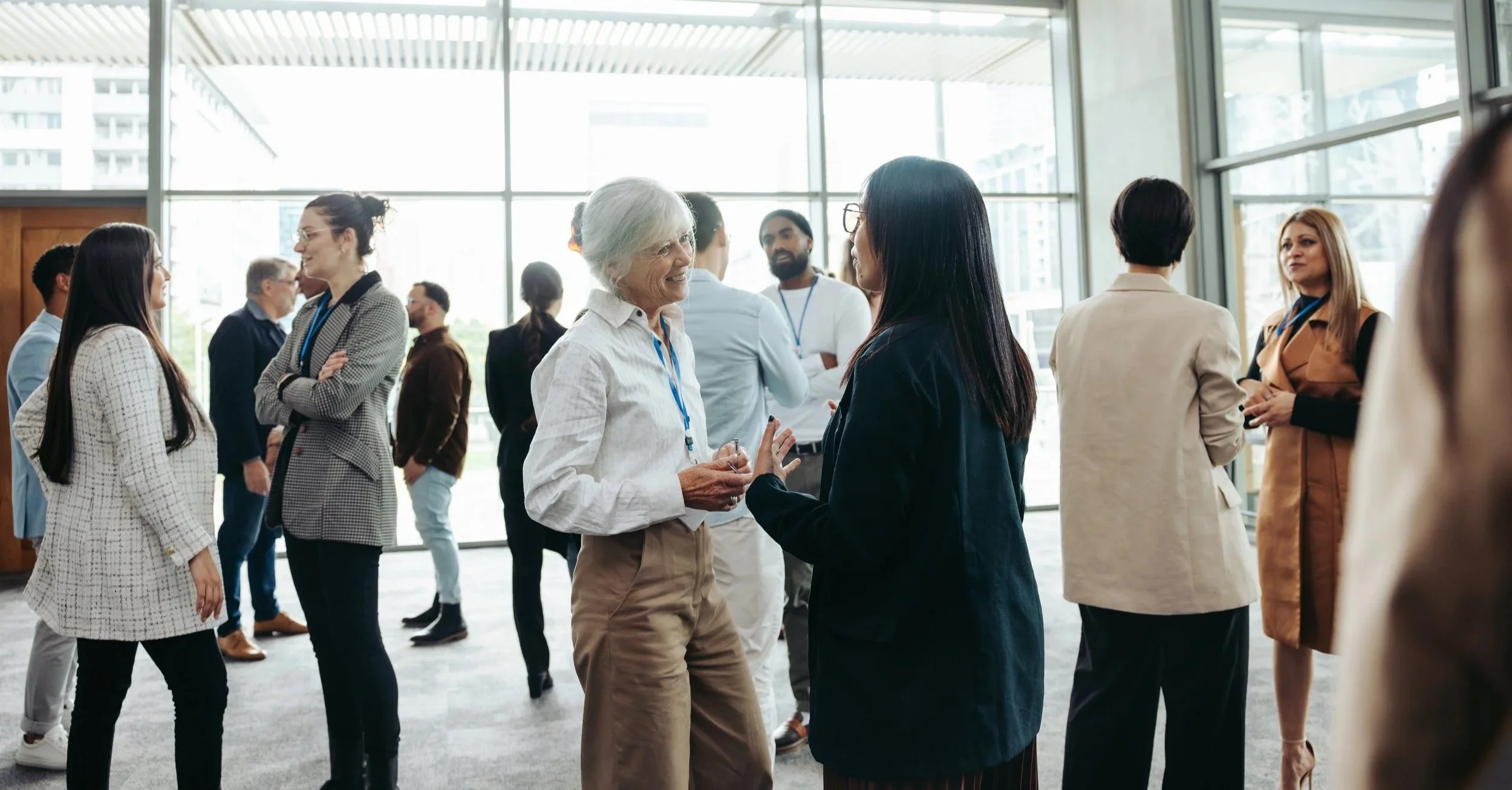 People engaged in conversations at a networking event in a modern indoor space with large windows.