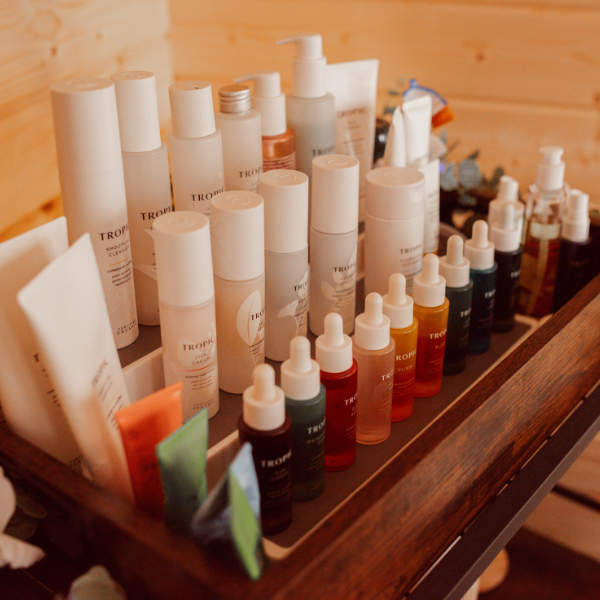 A wooden tray holding various skincare products, including bottles, tubes, and dropper bottles, arranged on a wooden surface.