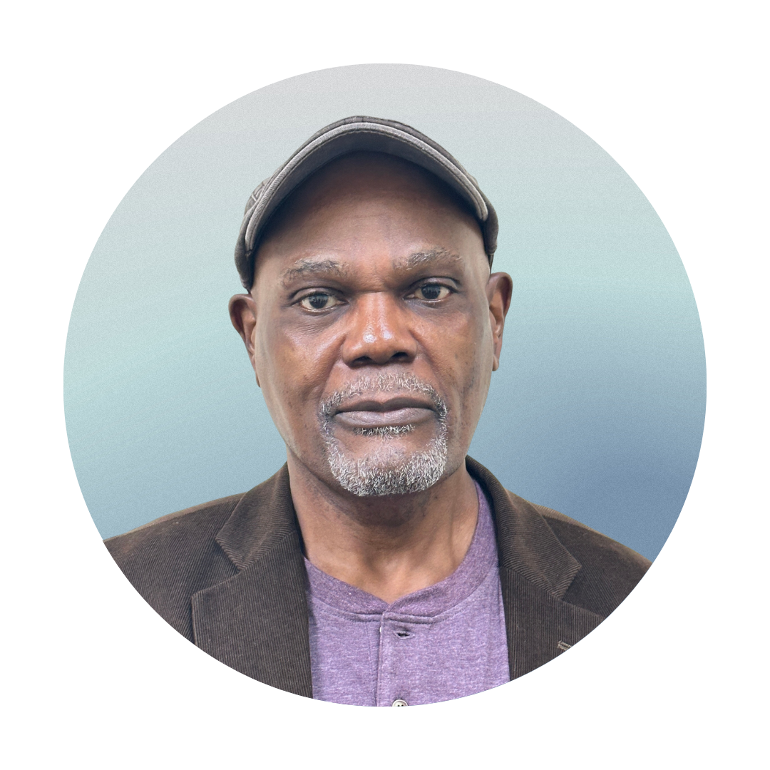 Portrait of a middle-aged man wearing a brown blazer, purple shirt, and a cap, against a gradient blue background.