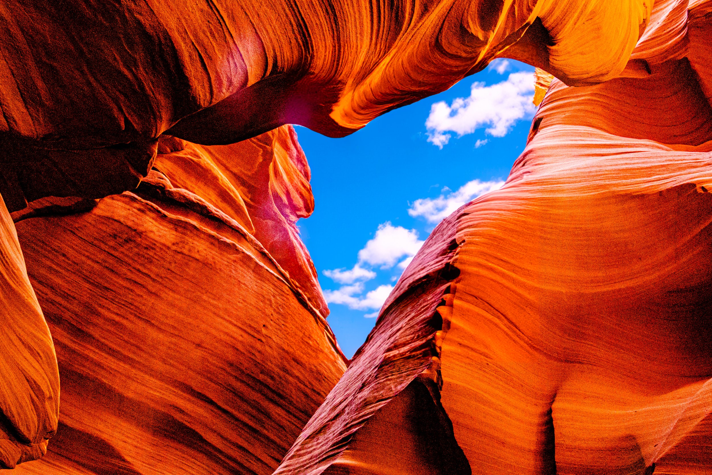 Vibrant red-orange sandstone canyon walls framing a blue sky with white clouds