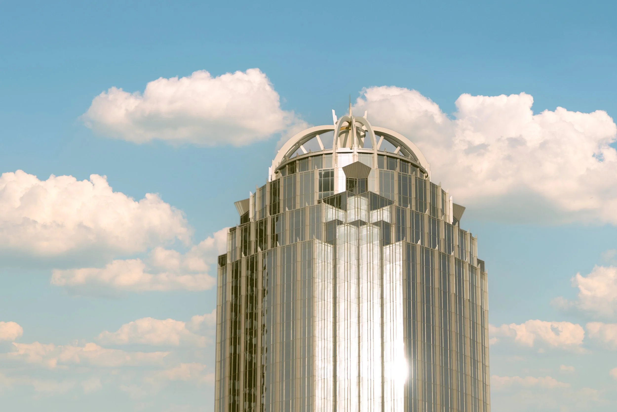 Modern glass skyscraper with an ornate domed rooftop against a blue sky with clouds