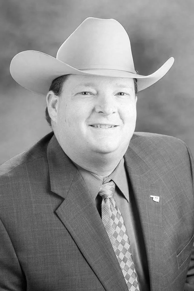 A man wearing a suit, tie, and cowboy hat, smiling in a professional portrait.