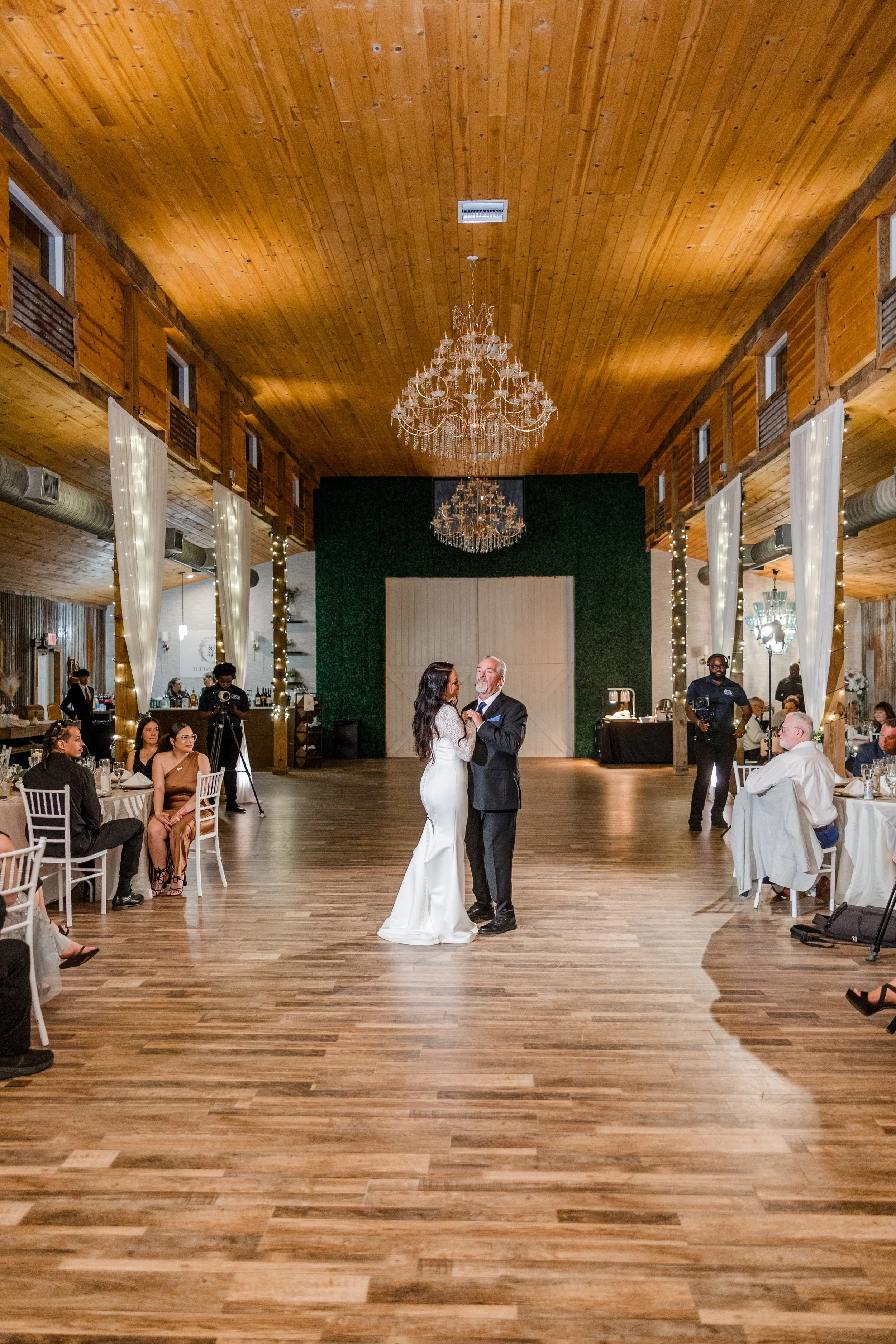 A bride and groom sharing a kiss outdoors, with vibrant pink flowers and lush greenery in the background.