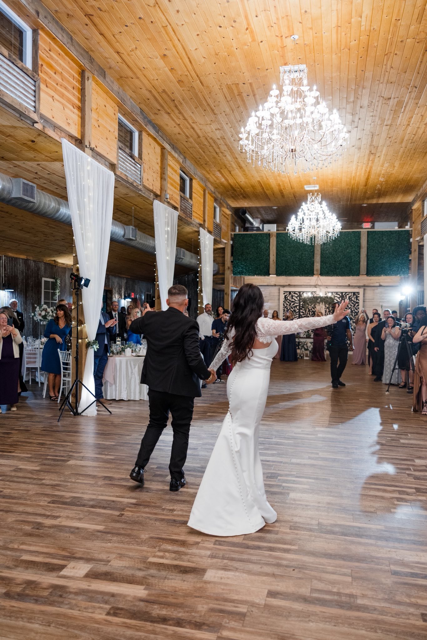 A bride and groom dancing at a wedding reception in a rustic venue with wooden walls and ceiling, chandeliers, and romantic lighting.