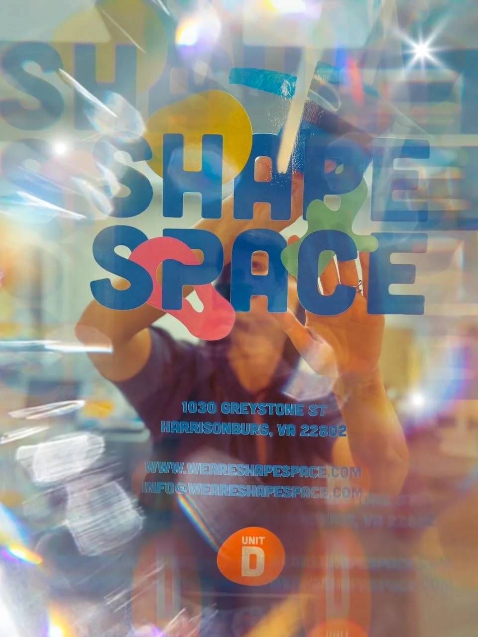 A colorful flyer for Shape Space at 1030 Greystone Street, Harrisonburg, VA 22602, with the website and email address, featuring an abstract multicolor star design and a person taking a photo of the flyer.