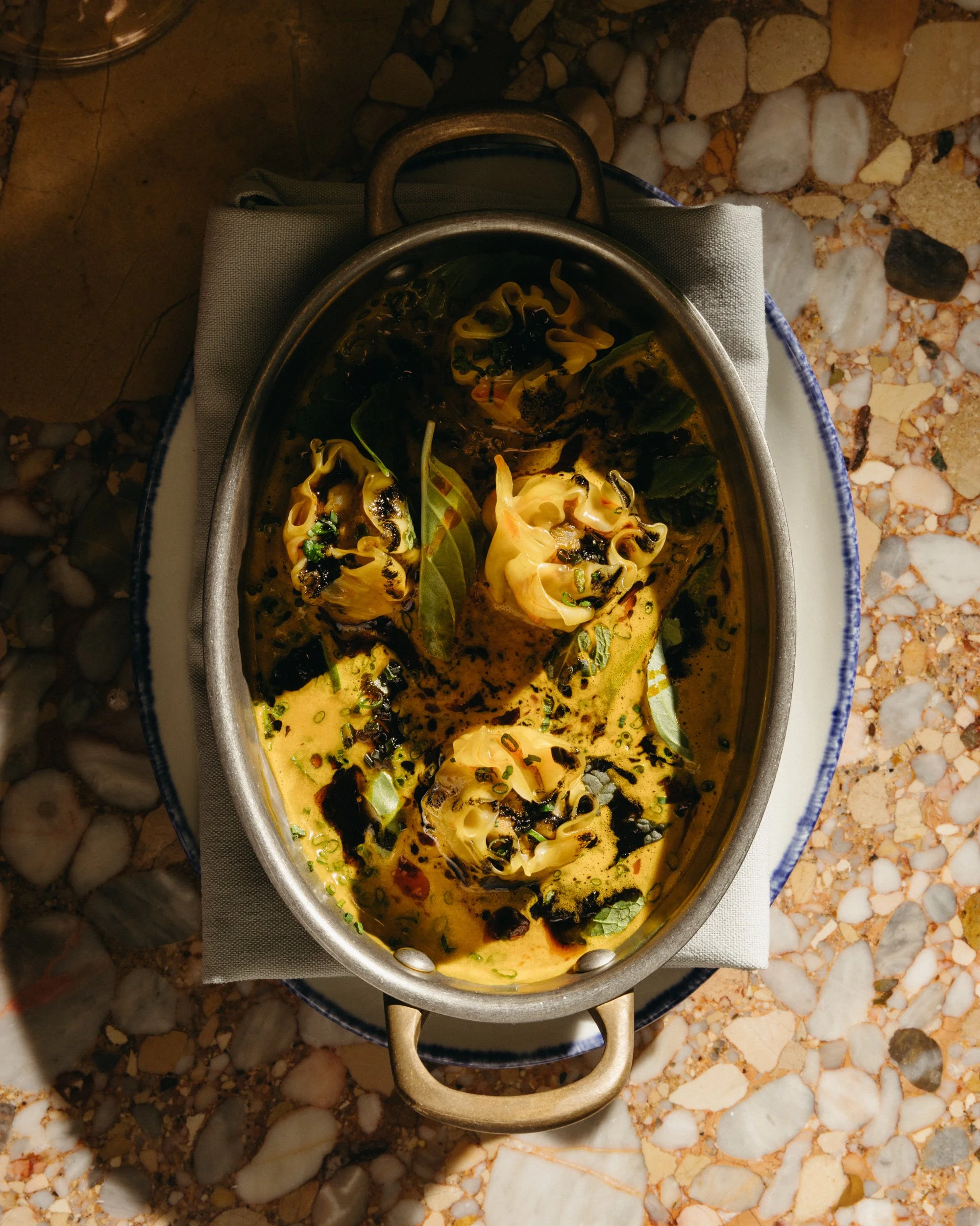 Shrimp dumplings with herbs and sauce, placed on a table with a stone and pebble surface.