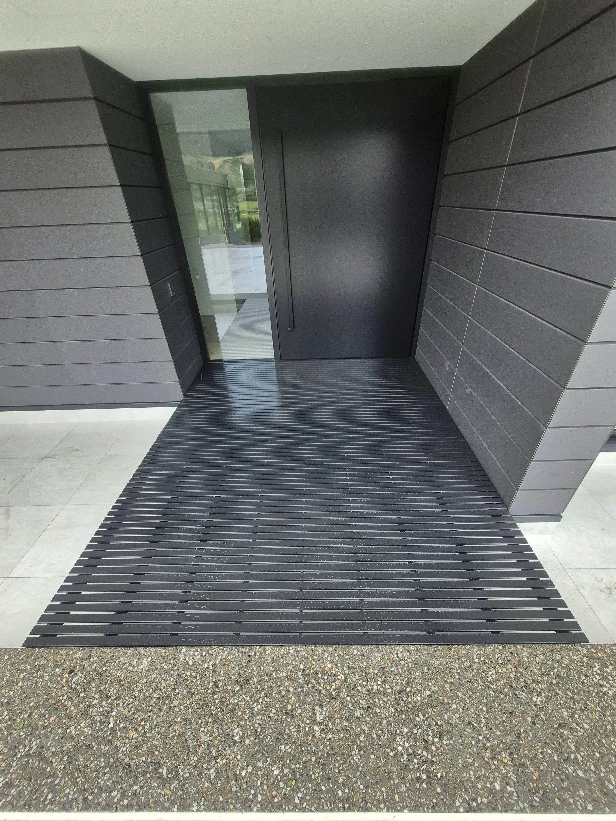Modern front entrance with black door, glass side panel, and black slatted porch