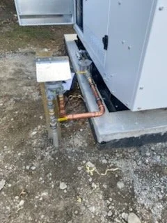 Outdoor electrical and plumbing setup next to a building foundation with piping and a small box.