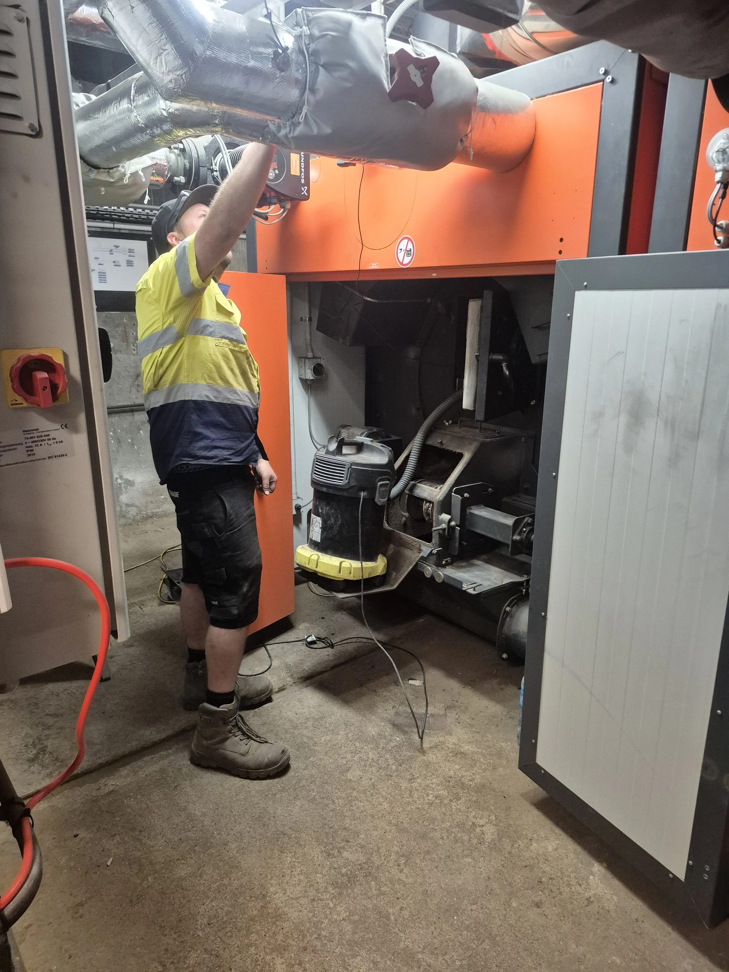 A worker in safety gear repairs machinery inside an industrial facility.