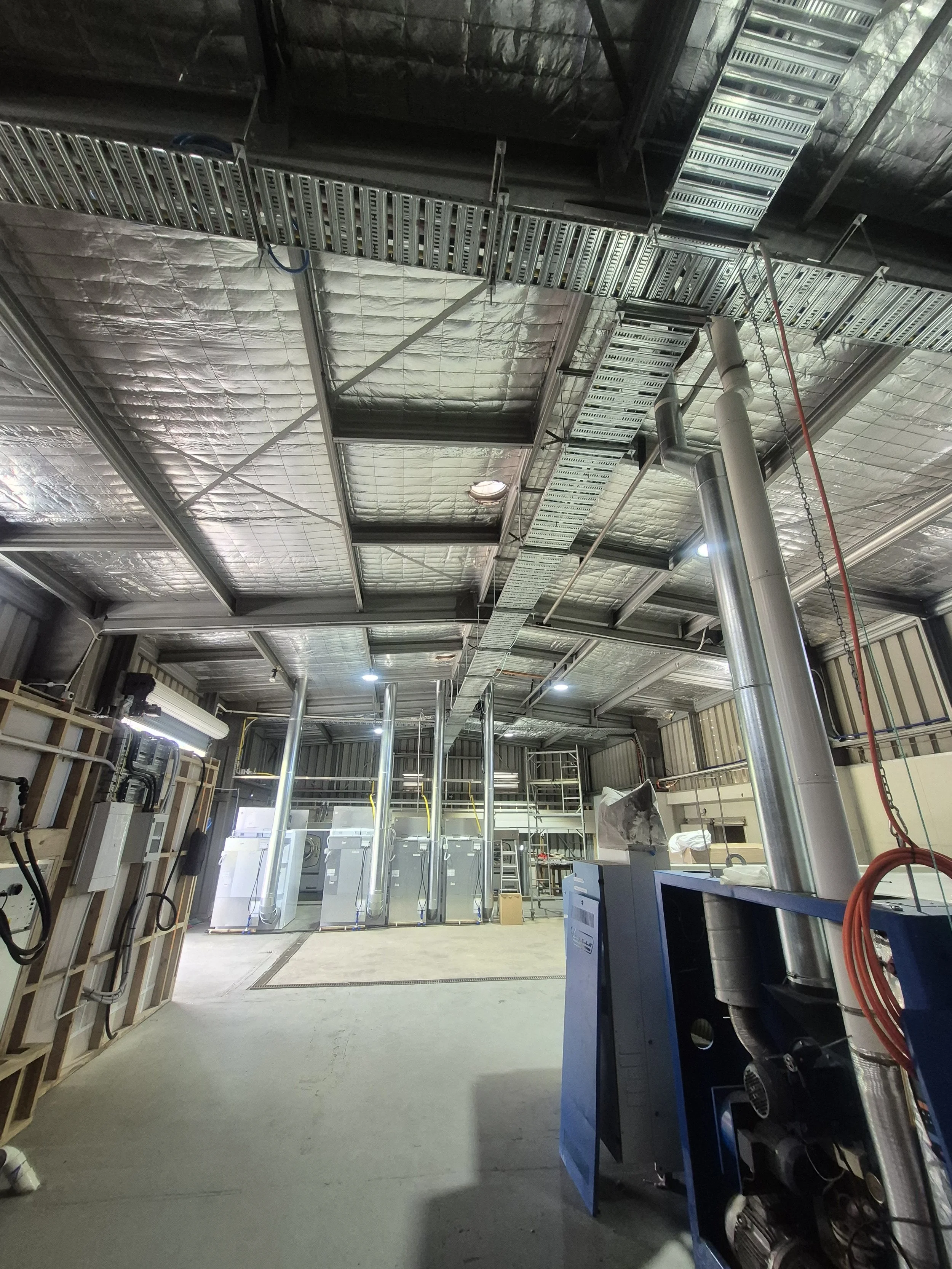 Construction site with exposed metal framework, insulation, and electrical conduits, revealing an unfinished interior of a building.