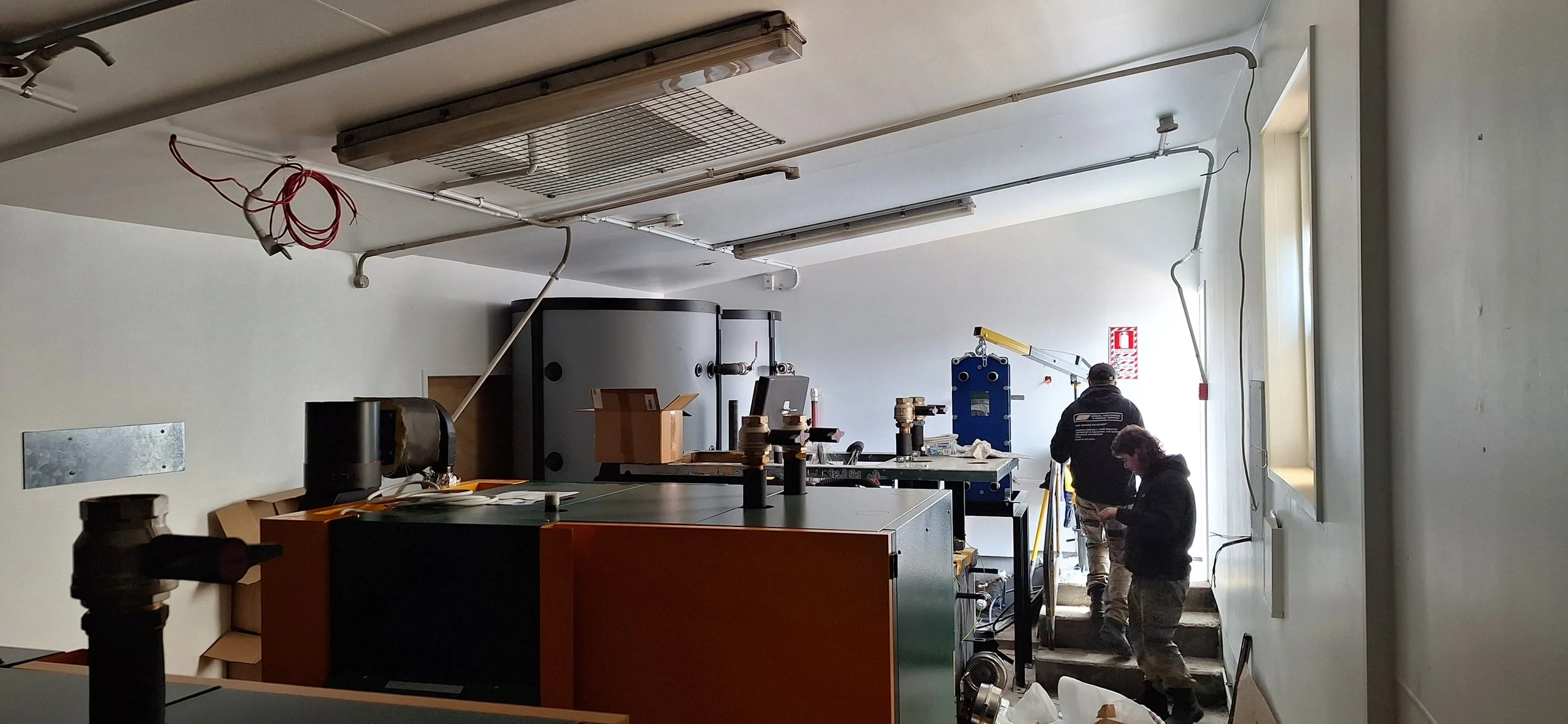 Interior of a room under renovation with construction workers, machinery, and electrical wiring on the ceiling.