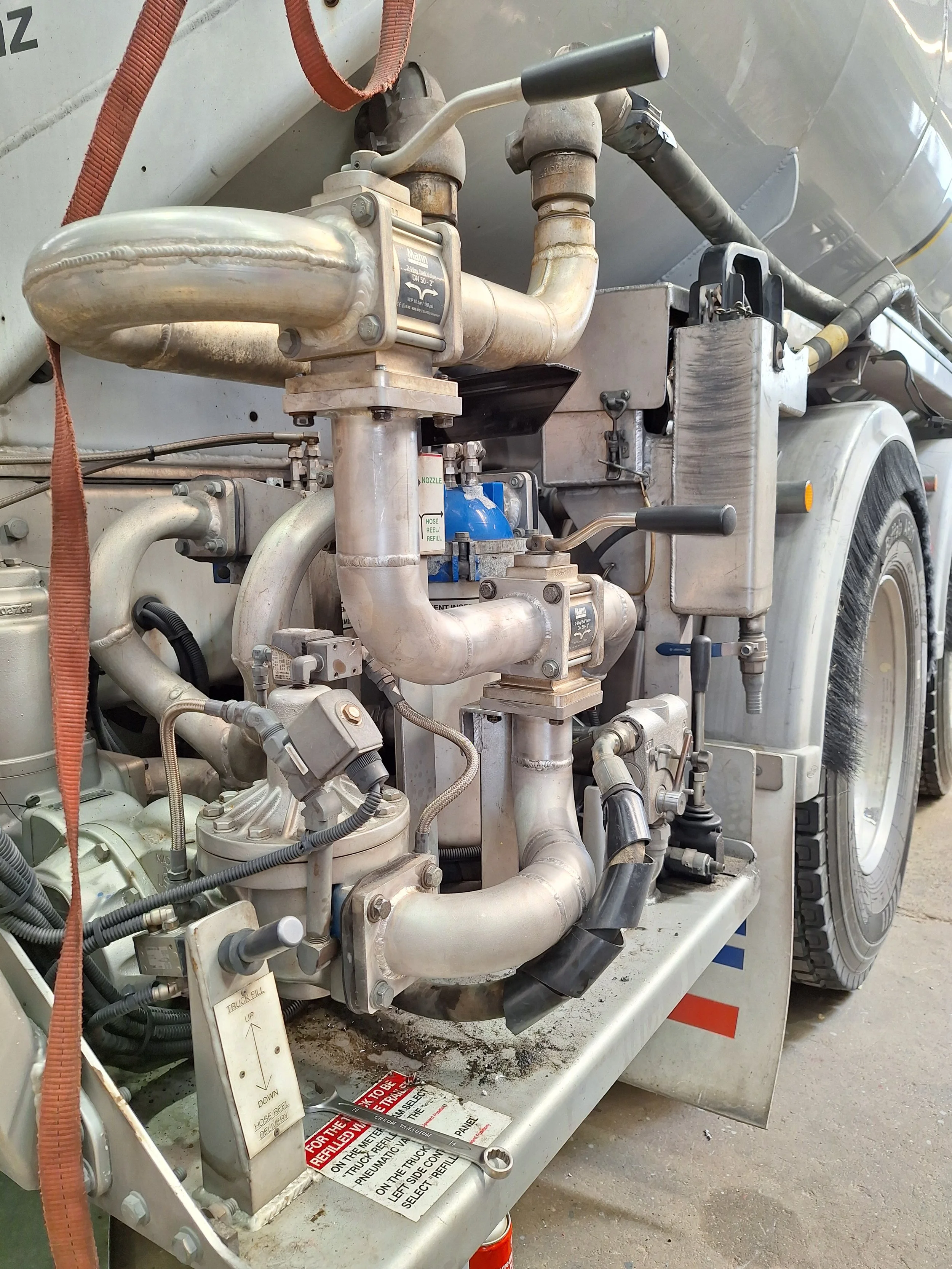 Close-up of machinery and pipes on a tanker truck, showing metal pipes, valves, and mechanical components.
