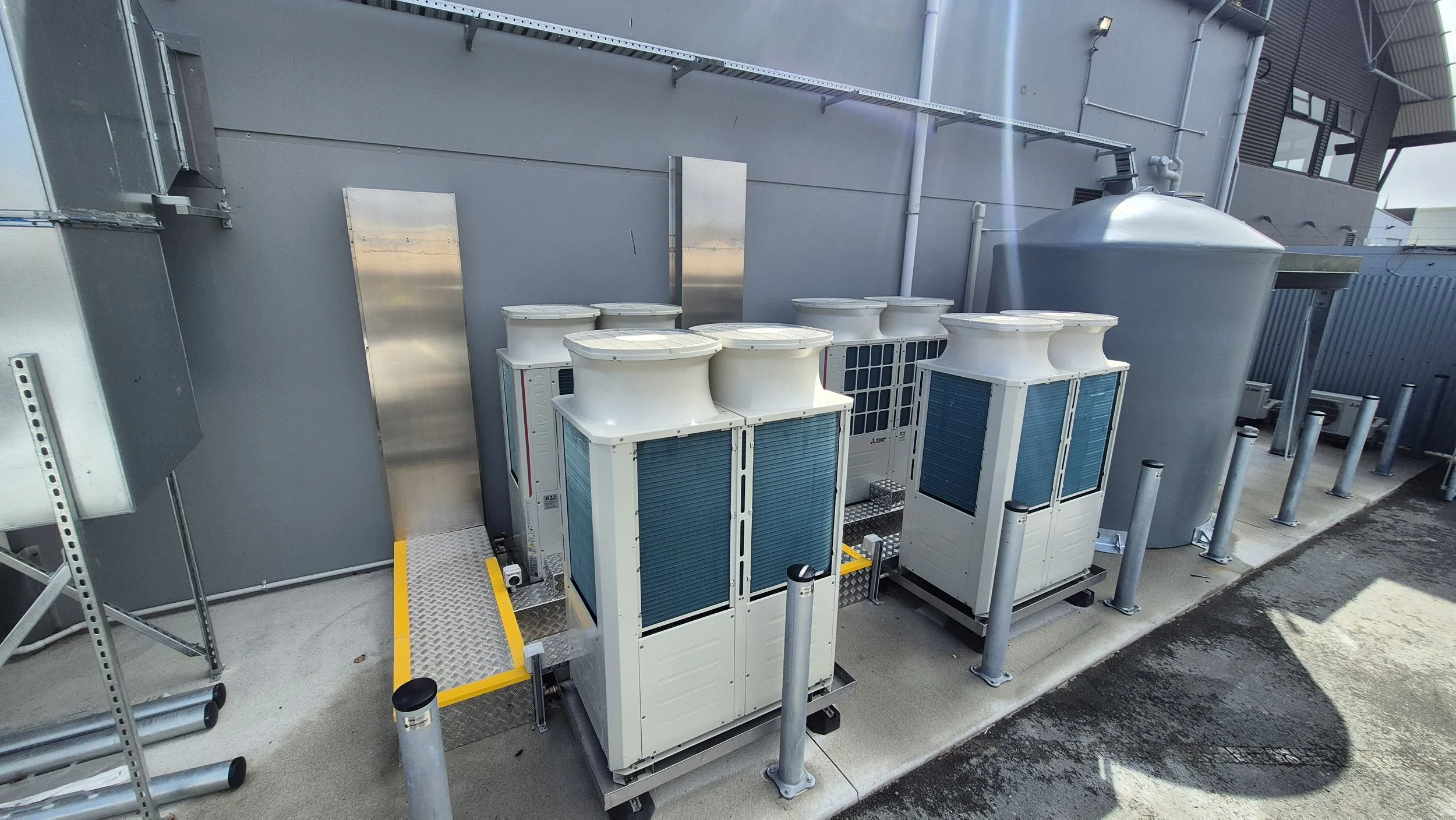 Industrial rooftop with HVAC units and large grey ventilation tank against a grey building wall.