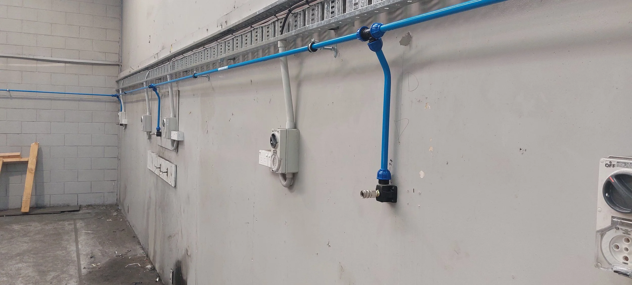 Electrical and plumbing wiring on a construction wall with blue plastic pipes, gray conduit boxes, and electrical outlets.