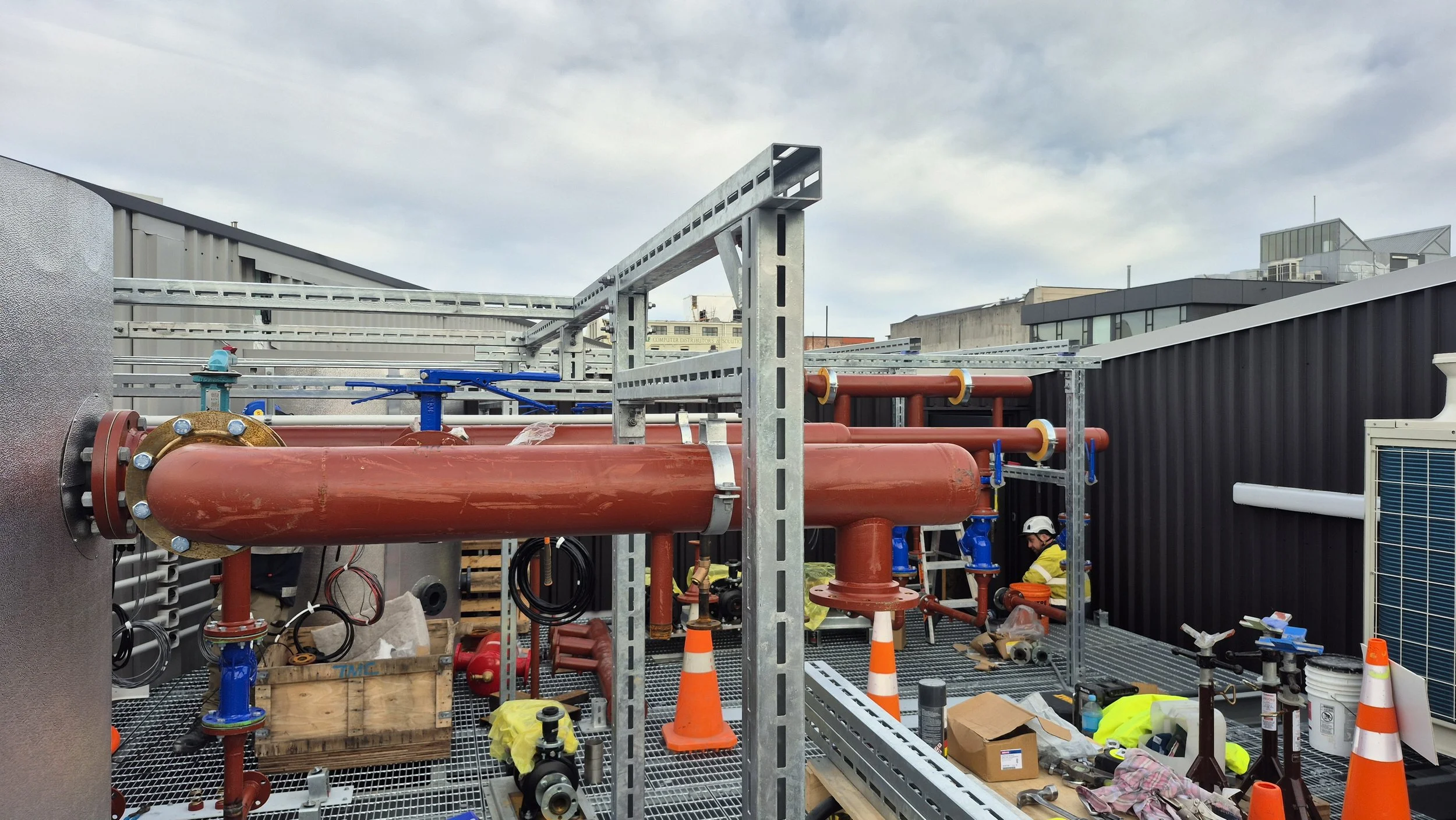 Infrared pipes and equipment installation on a rooftop, with workers and construction tools, in an urban area.