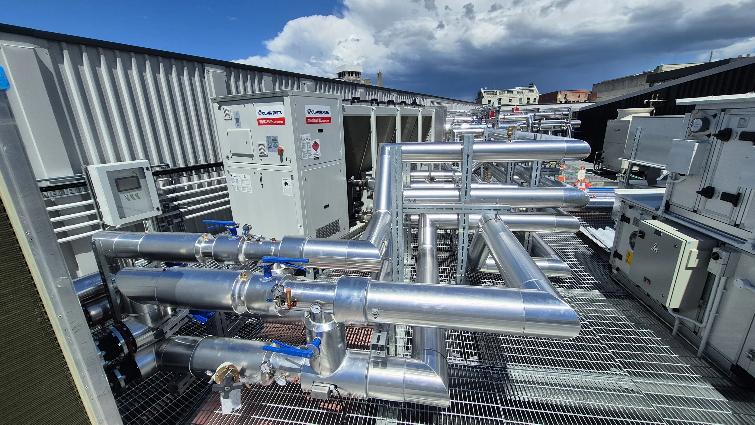  rooftop with industrial HVAC system featuring extensive silver piping, control panels, and electrical equipment, set against a partly cloudy sky.