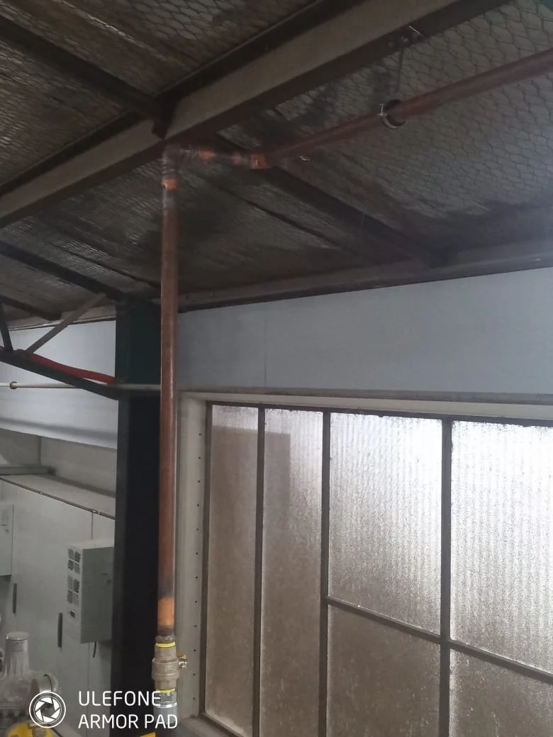 Indoor space with metallic ceiling, a large vertical pipe, and a frosted glass window
