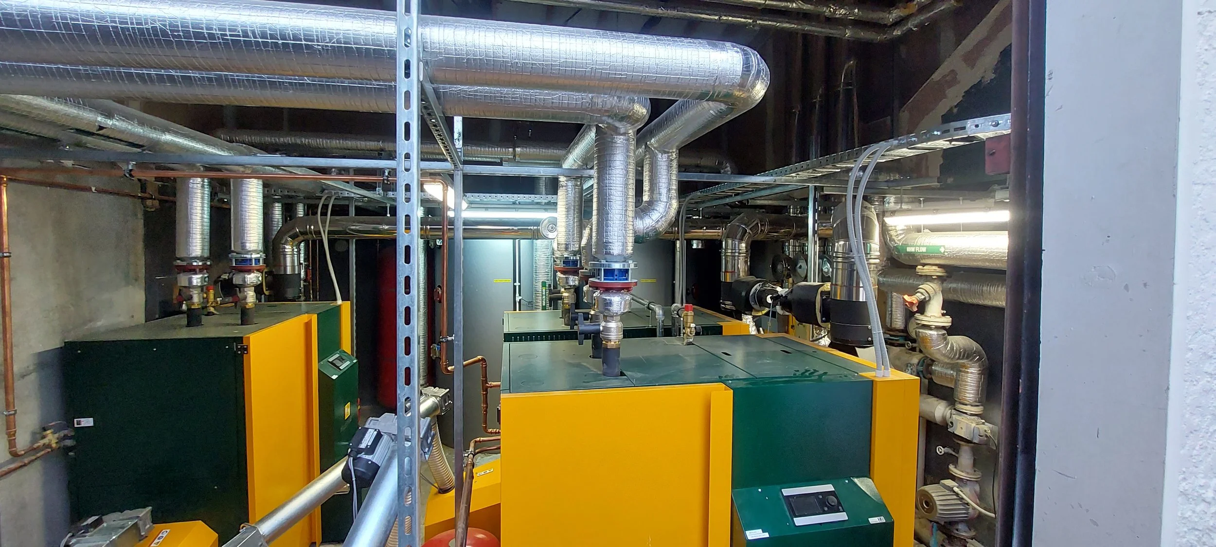 Industrial equipment including yellow and green machinery with metal pipes and gauges in a utility room.