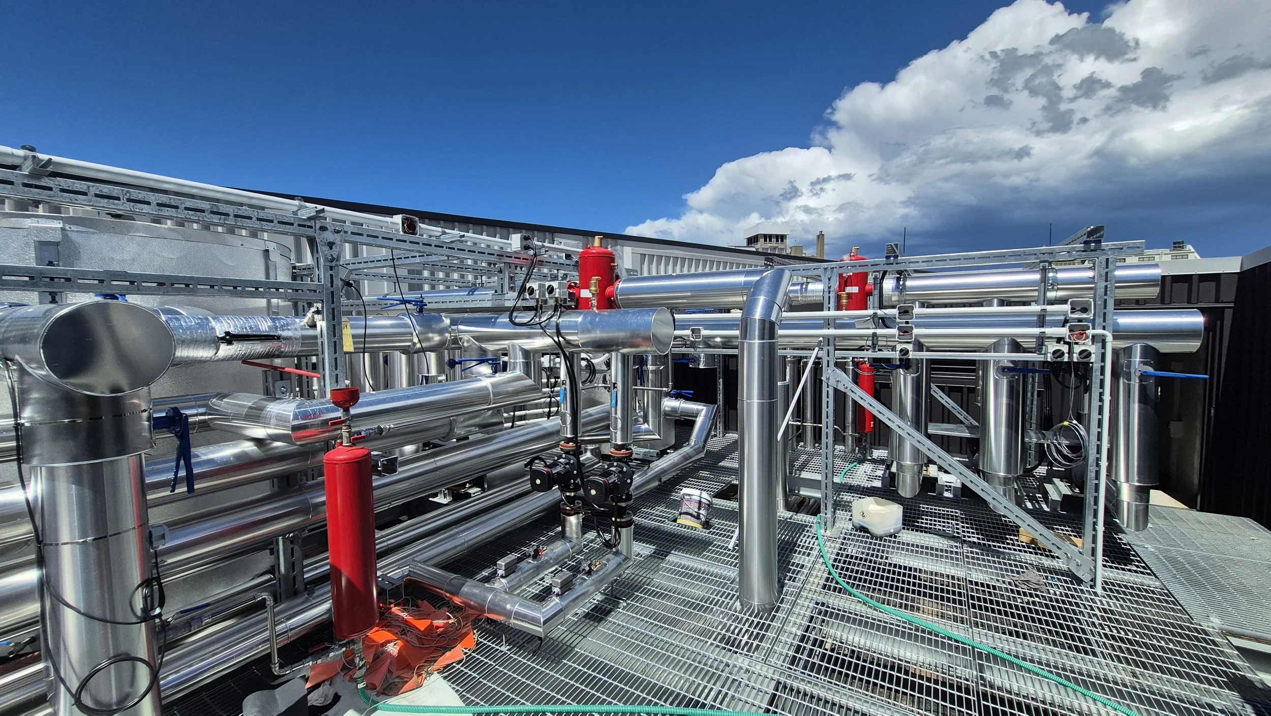 Industrial rooftop with metal pipes, valves, and machinery under a partly cloudy sky.